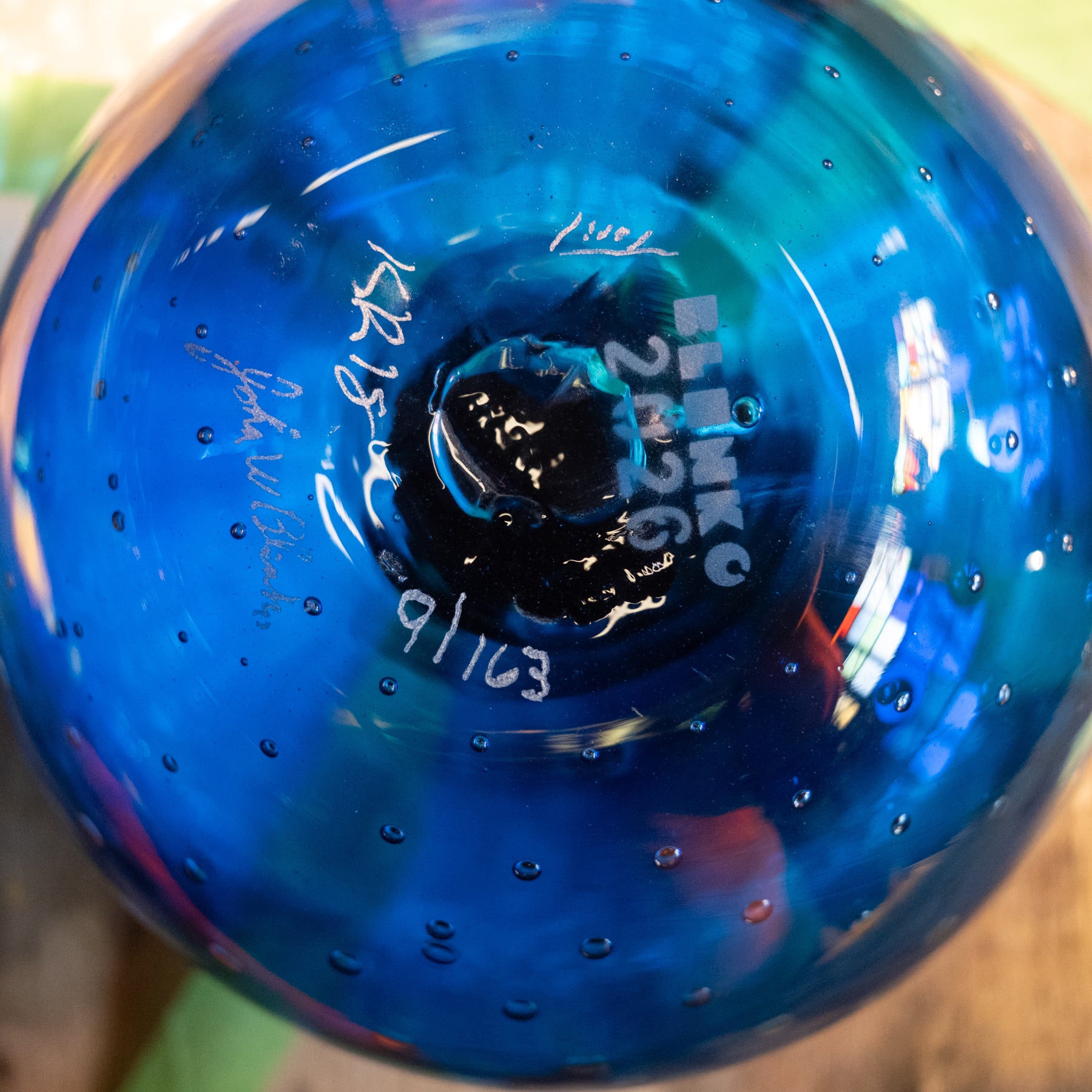 Close-up of the bottom of a blue glass bowl with white hand-written markings and bubble details, showing the maker's signature and numbers.
