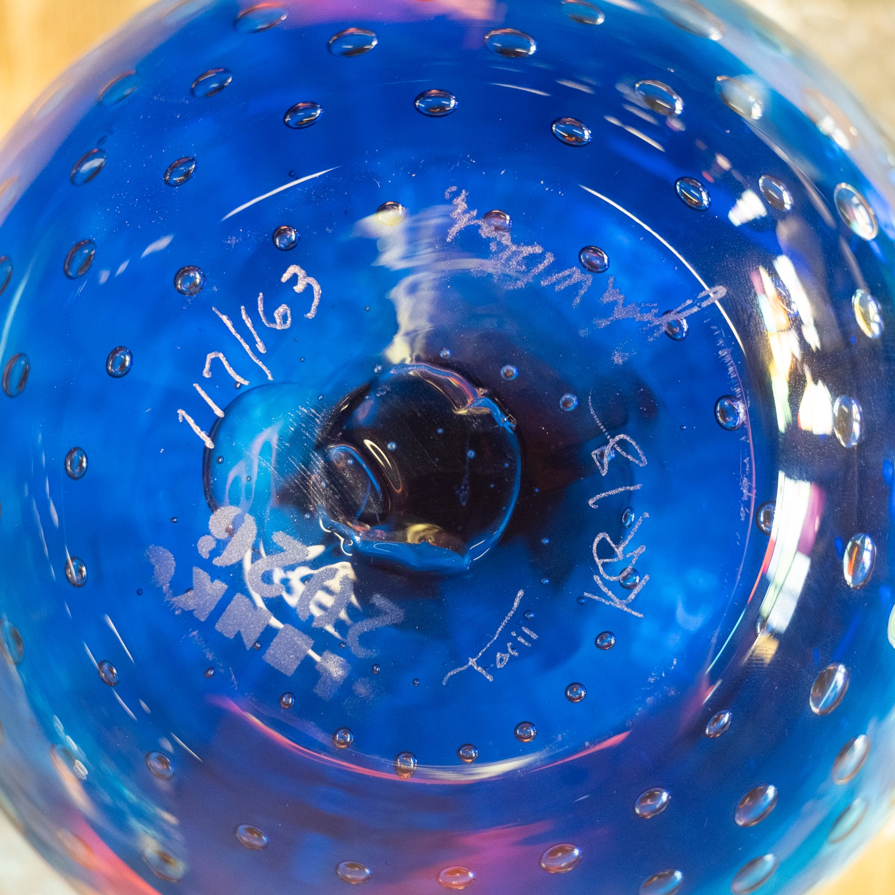 A close-up of a vibrant blue glass bowl with a textured, bubbled surface and hand-written white ink markings inside.