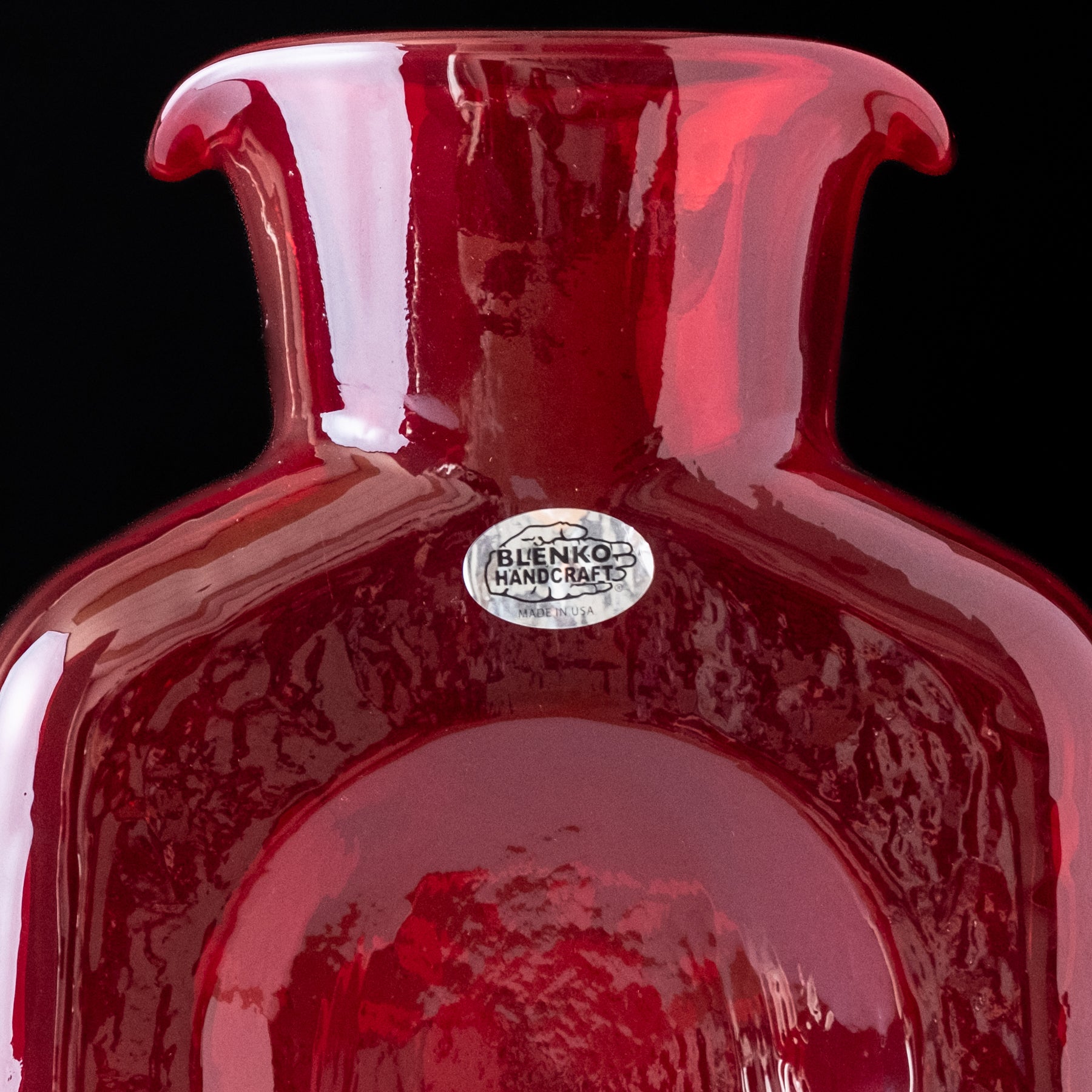 Red glass vase with a visible brand label on a black background