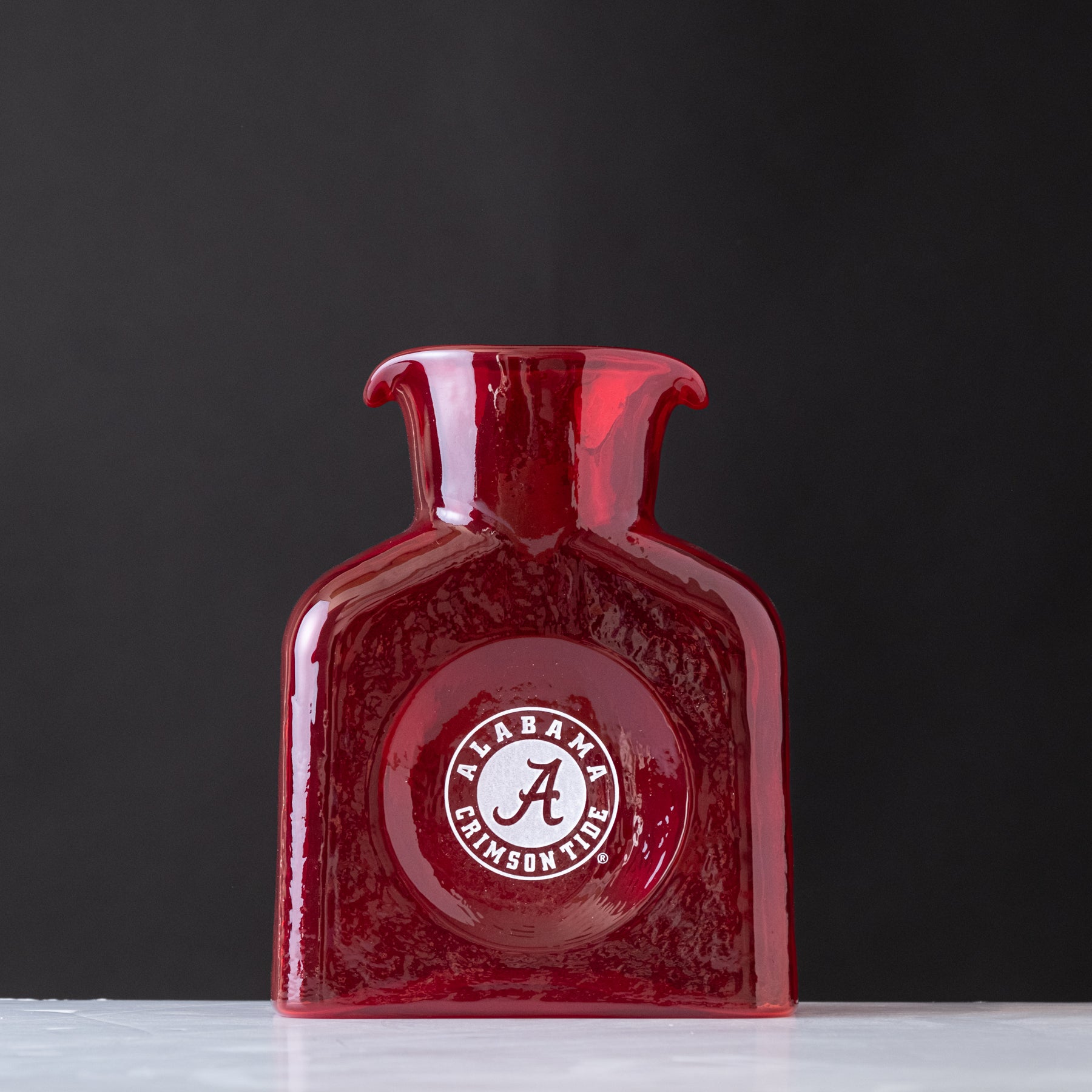 Red glass vase with Alabama Crimson Tide logo on a dark background