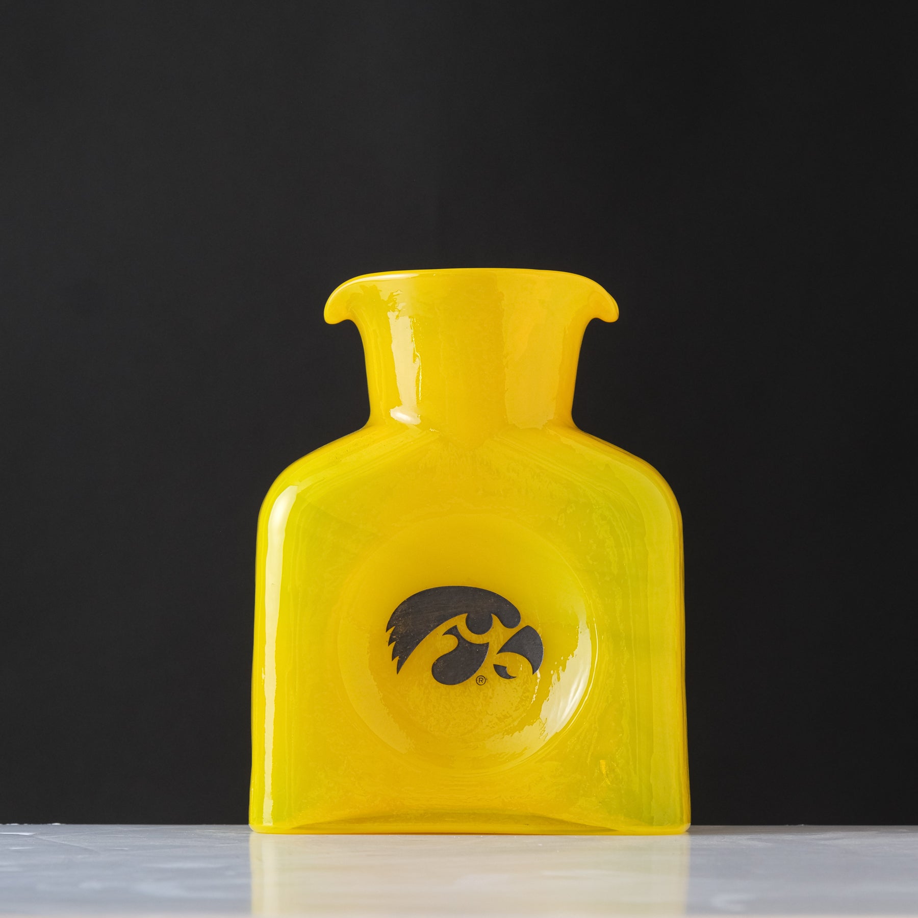 Yellow glass vase with a black logo on a dark background