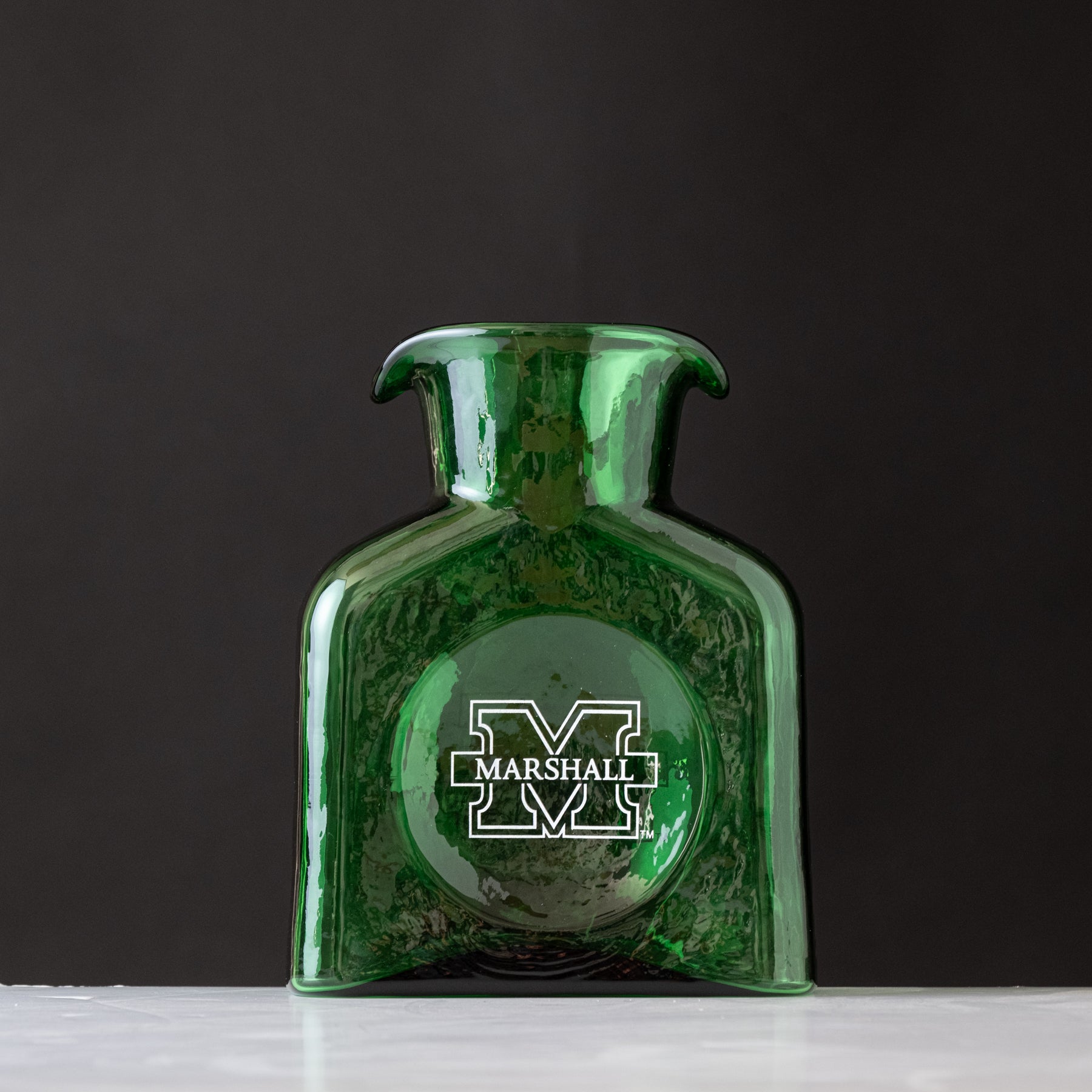 Green glass vase with Marshall University logo on a dark background