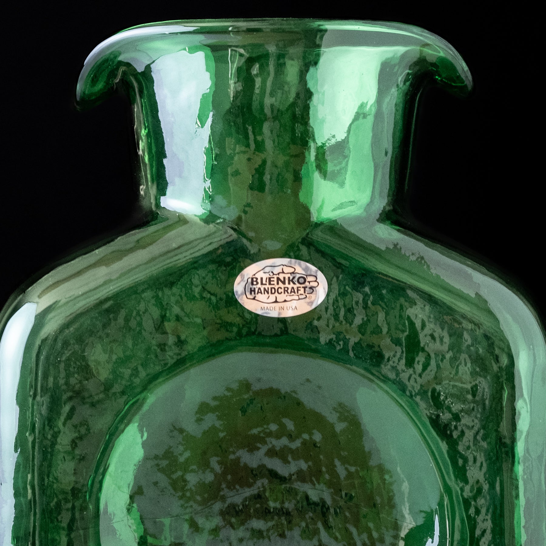 Green glass vase with a visible brand label on a black background