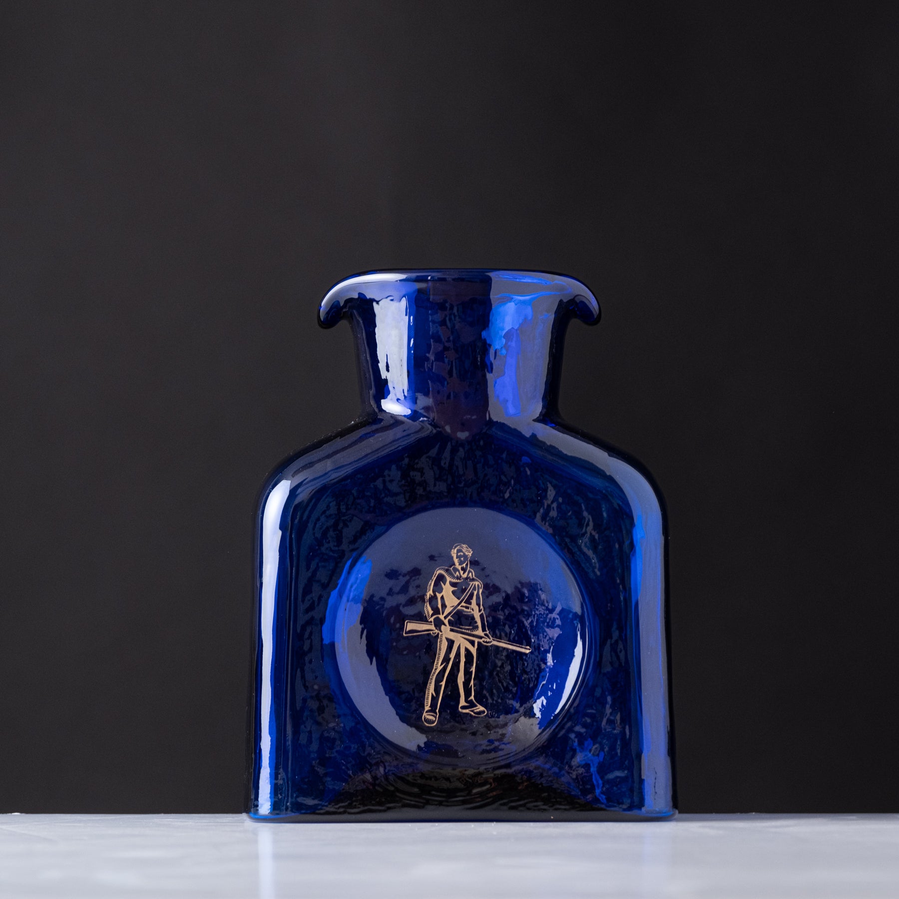 Blue glass bottle with gold emblem on a dark background