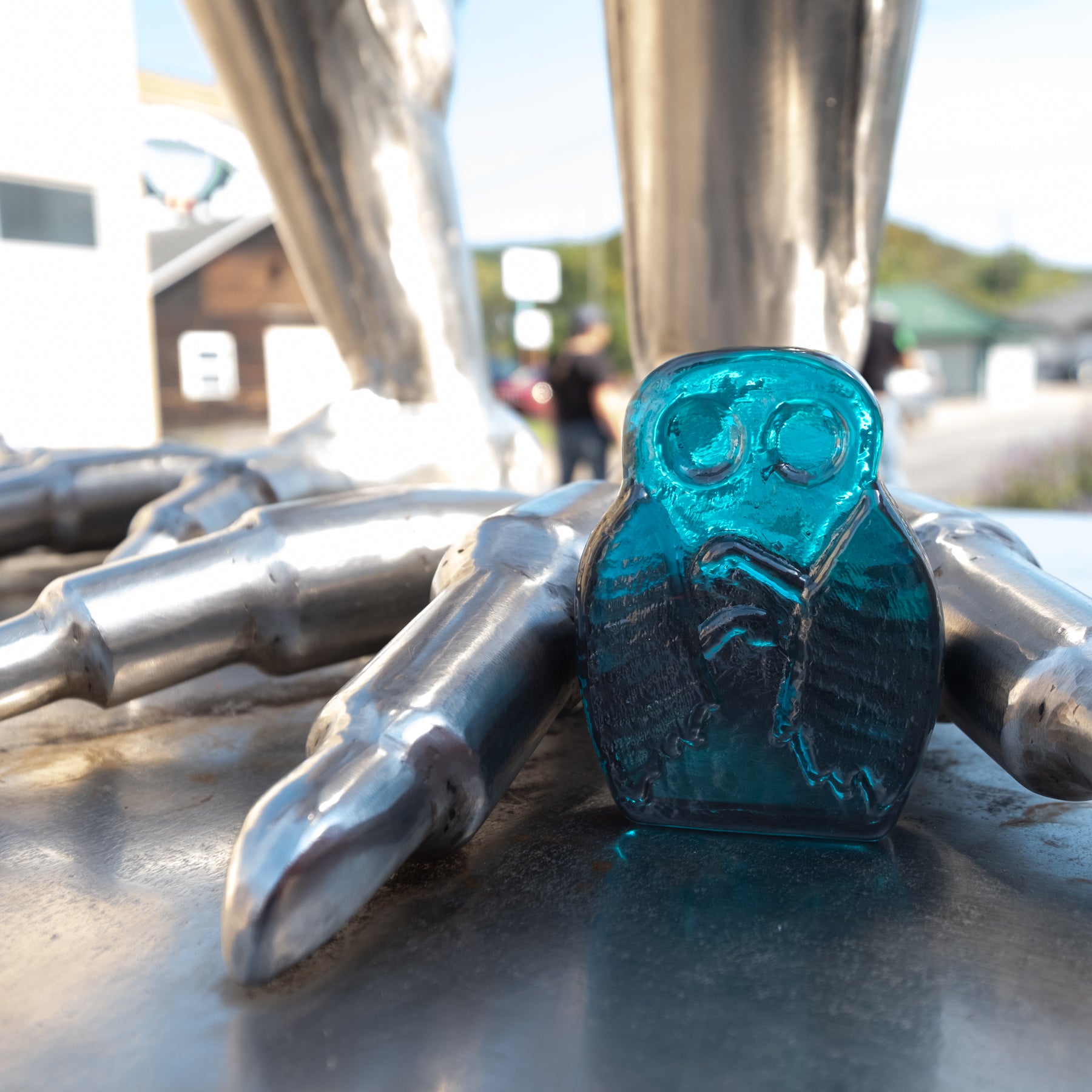 Blue glass owl figurine among metal objects with a blurred outdoor background