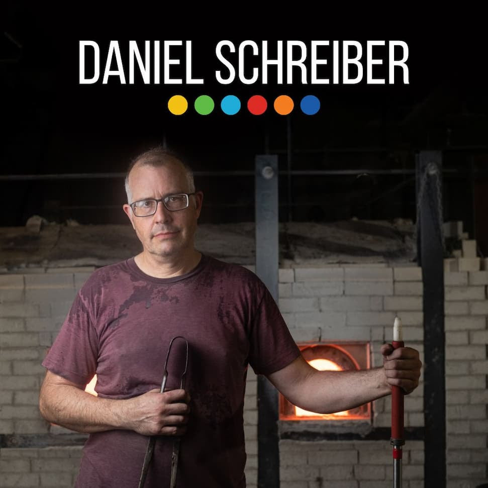 Man holding glassblowing tools with 'Daniel Schreiber' text above in a workshop setting