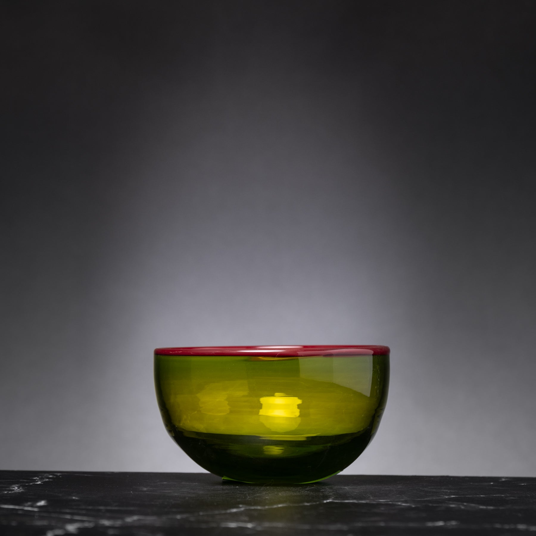 Green glass bowl with red rim on a dark surface against a gray background