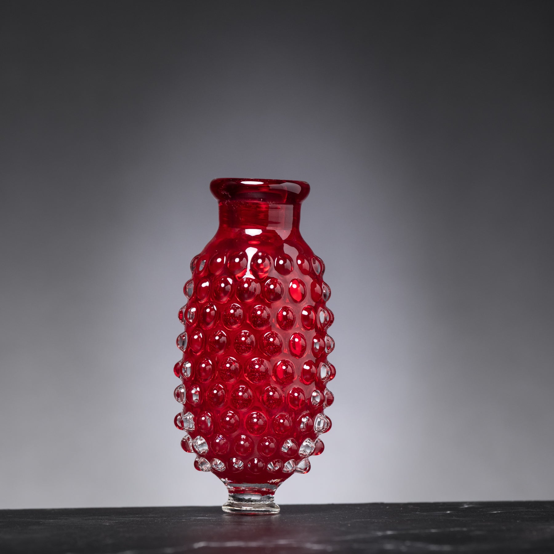 Red glass vase with a textured surface on a dark surface and gray background