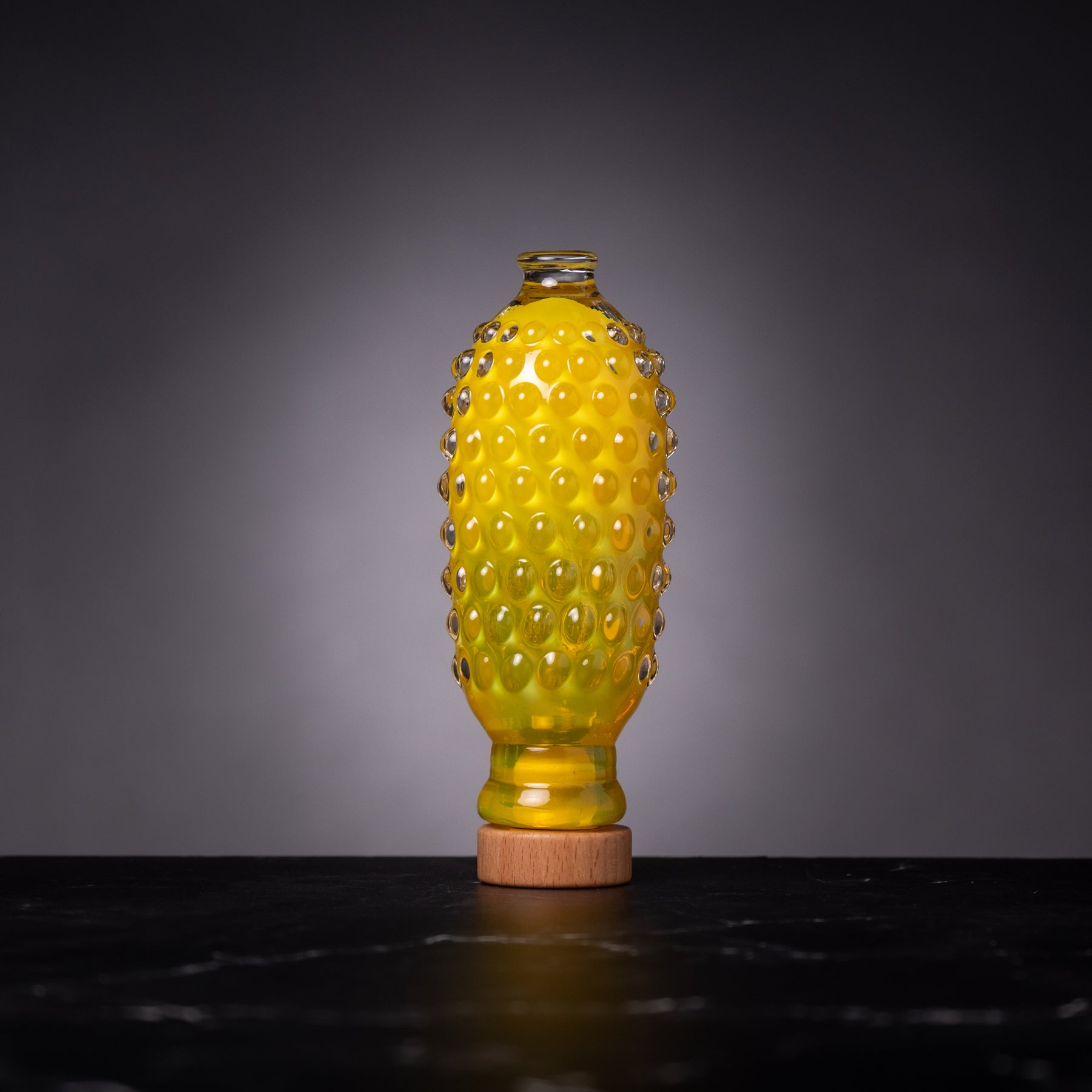 Yellow glass bottle with textured surface on a dark surface and gray background