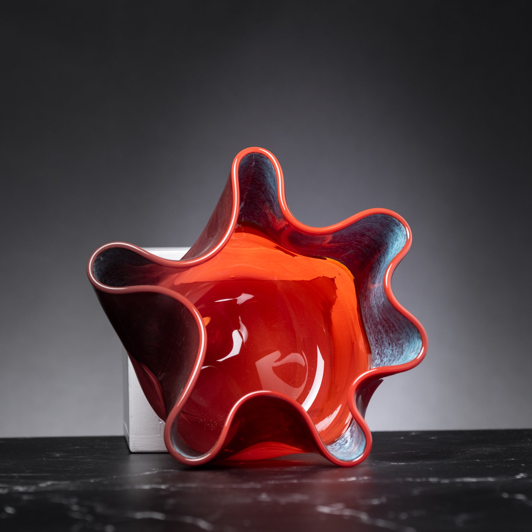 Red ceramic vase with wavy design on a dark surface and gray background