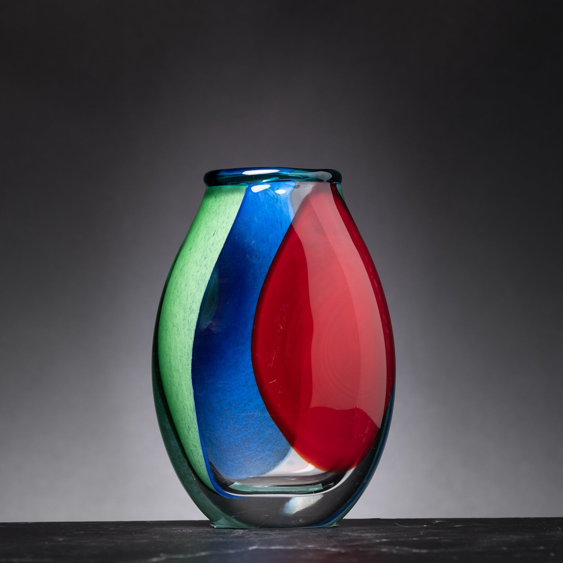 Colorful glass vase with green, blue, and red segments on a dark background
