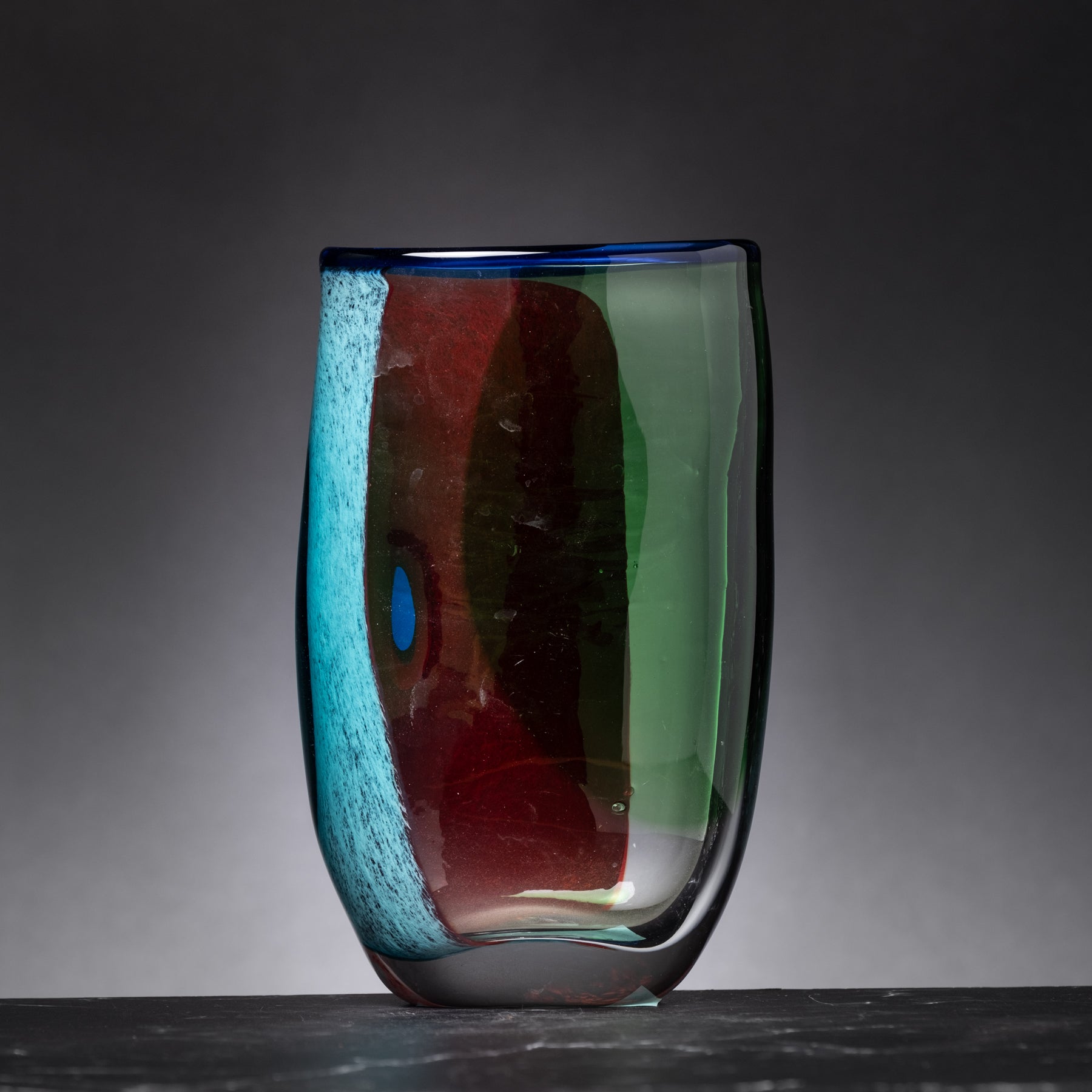 Colorful glass vase with blue, red, and green hues on a dark background