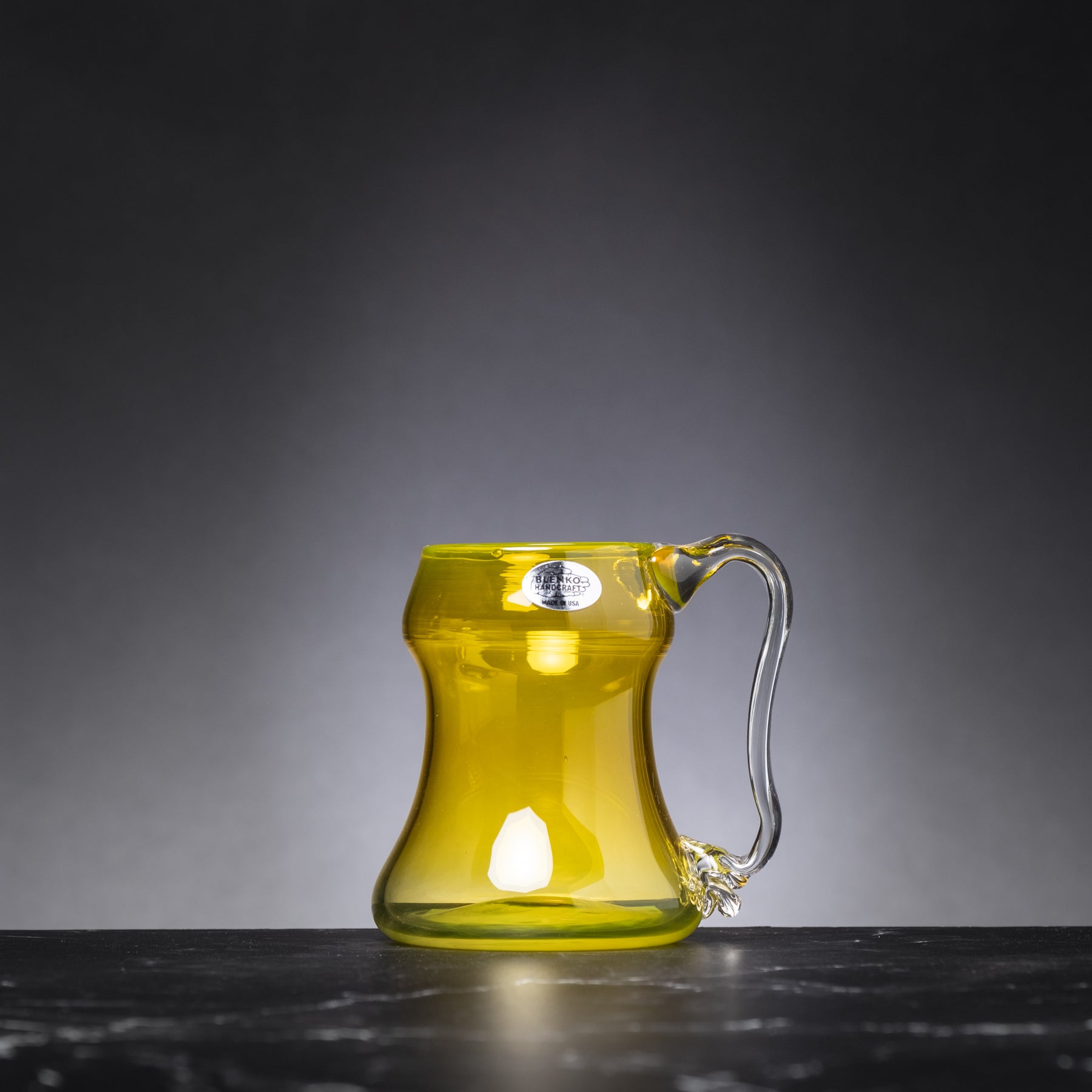Yellow glass mug with handle on a dark surface and gray background