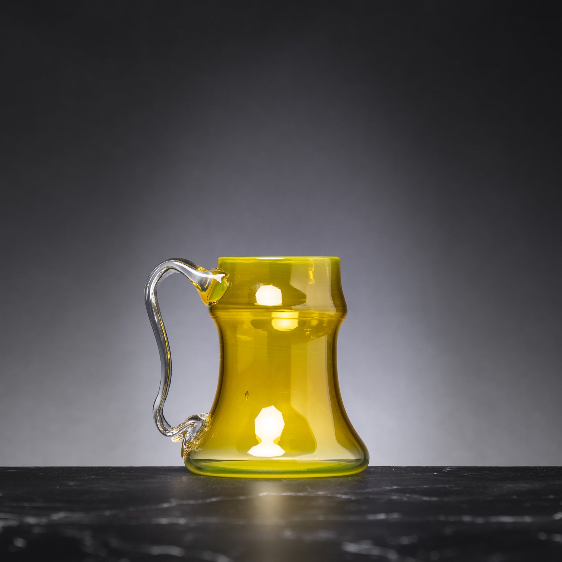 Yellow glass mug with handle on a dark surface and gray background