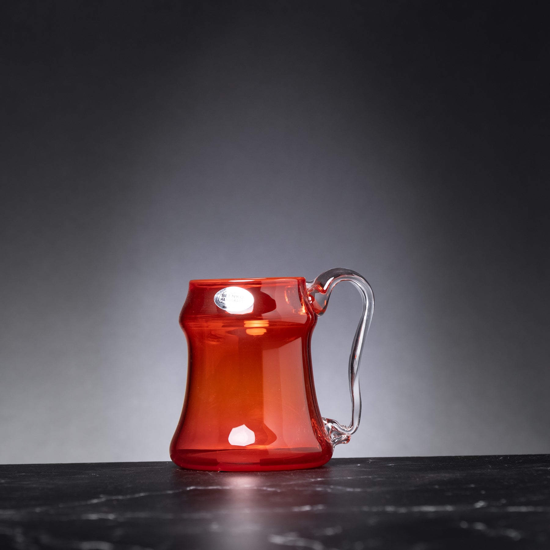 Red glass mug with a clear handle on a dark surface and gray background