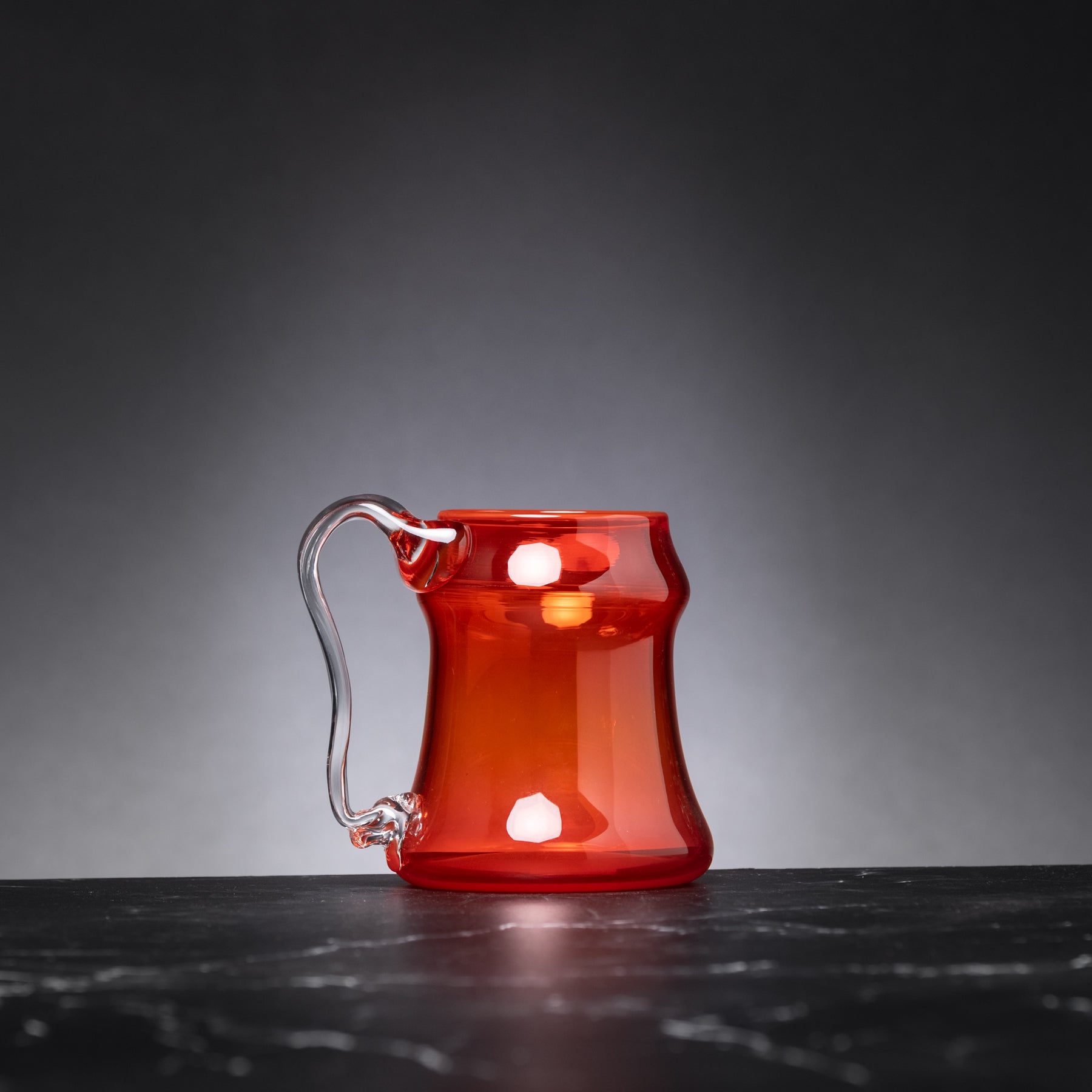 Red glass mug with a handle on a dark surface and gray background
