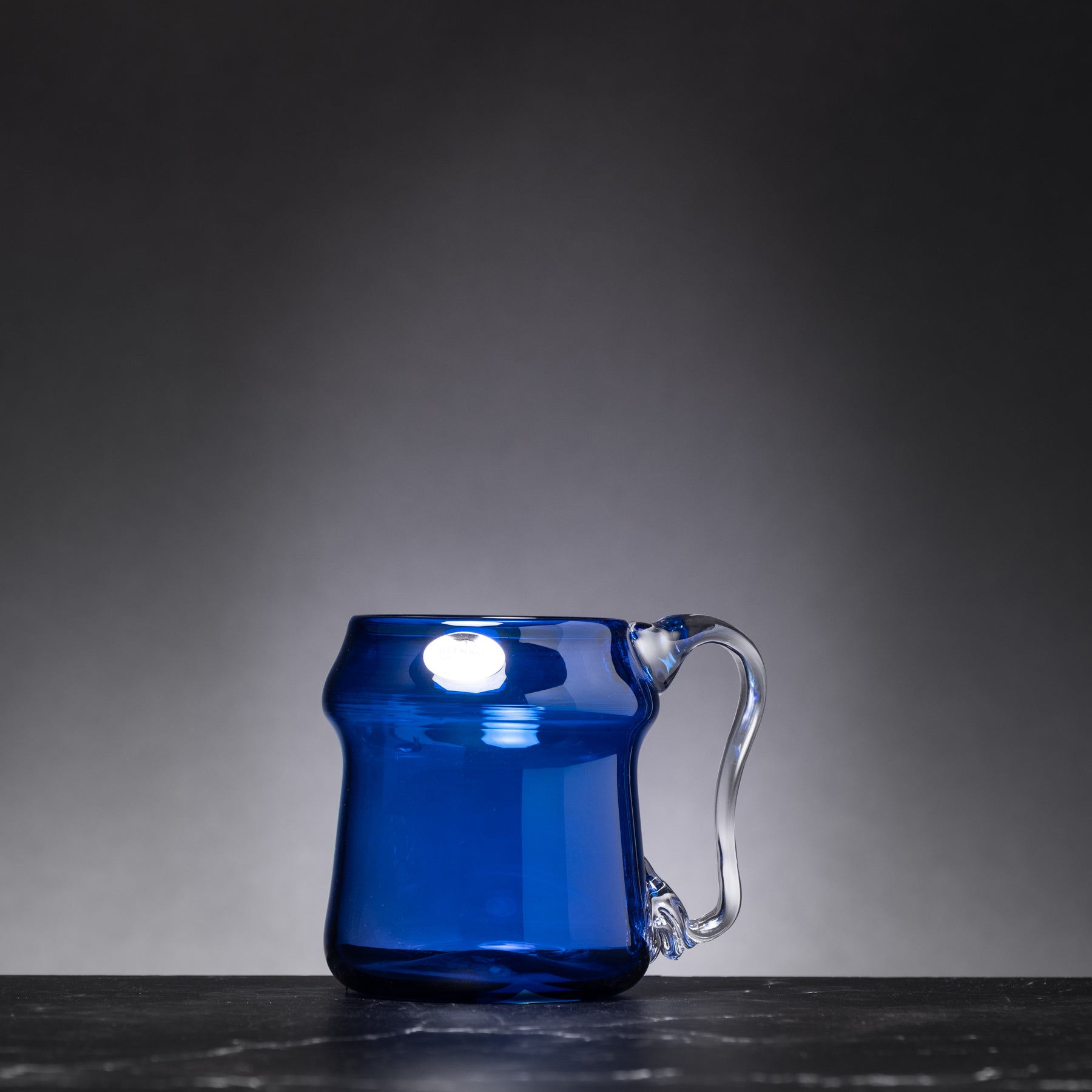 Blue glass mug on a dark surface with a gray background