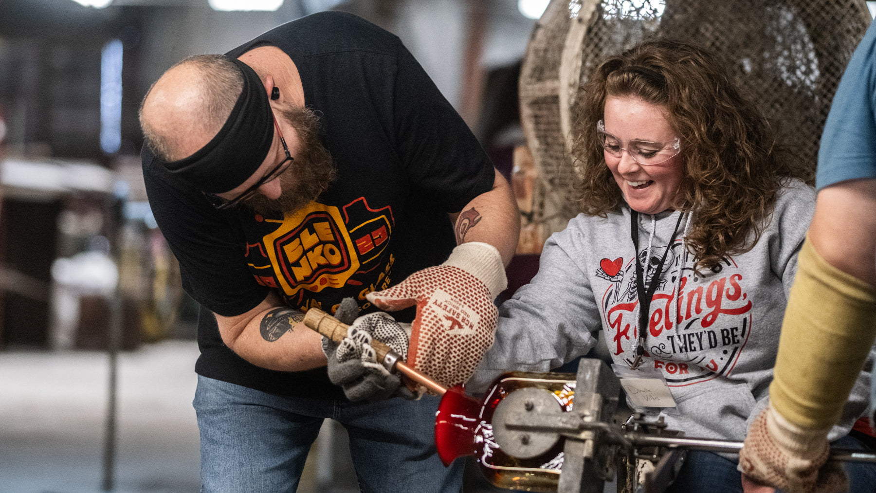 Two people working together on a project, one wearing a black shirt with a logo and the other in a gray shirt with text.