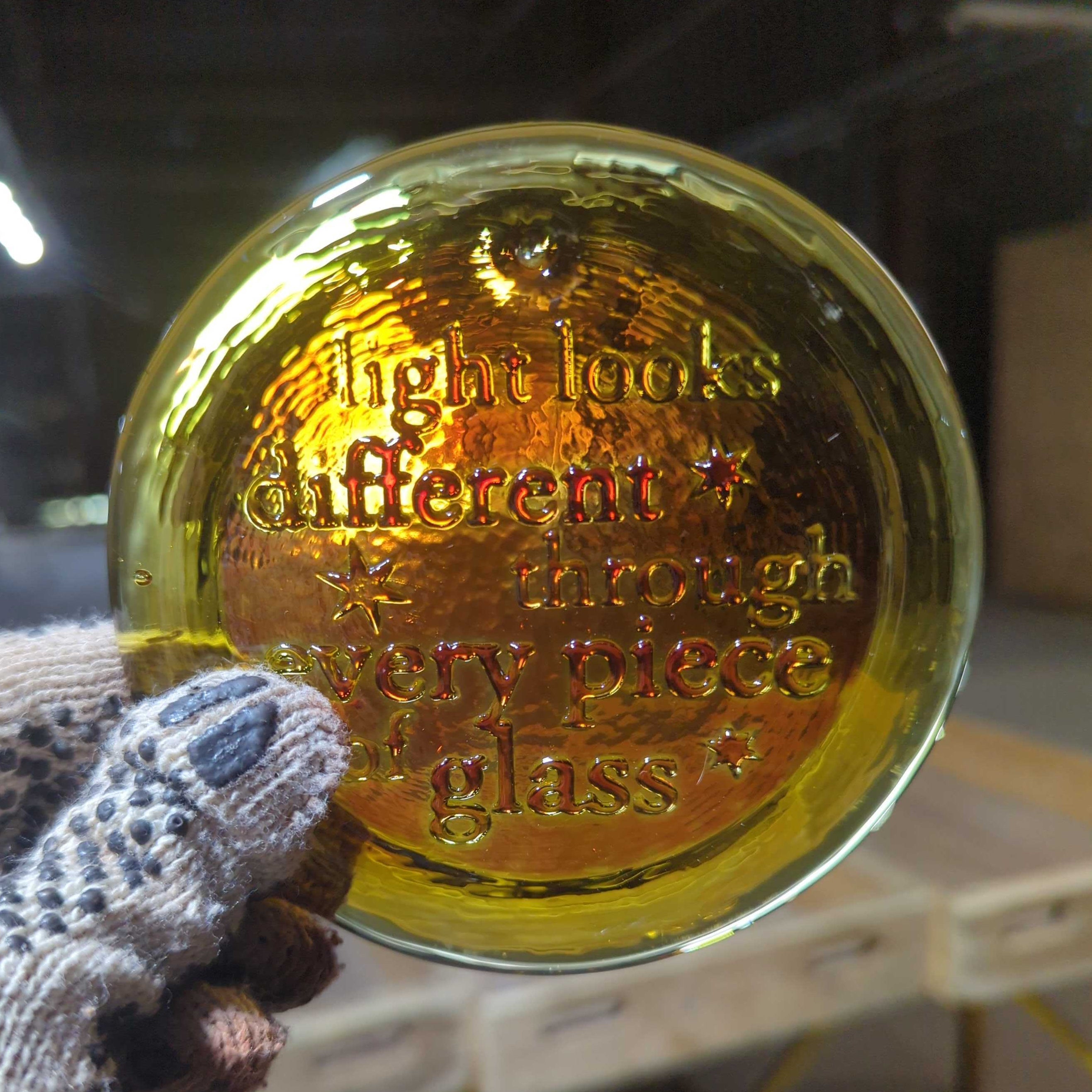 Gold glass sphere with text held by a gloved hand in an indoor setting