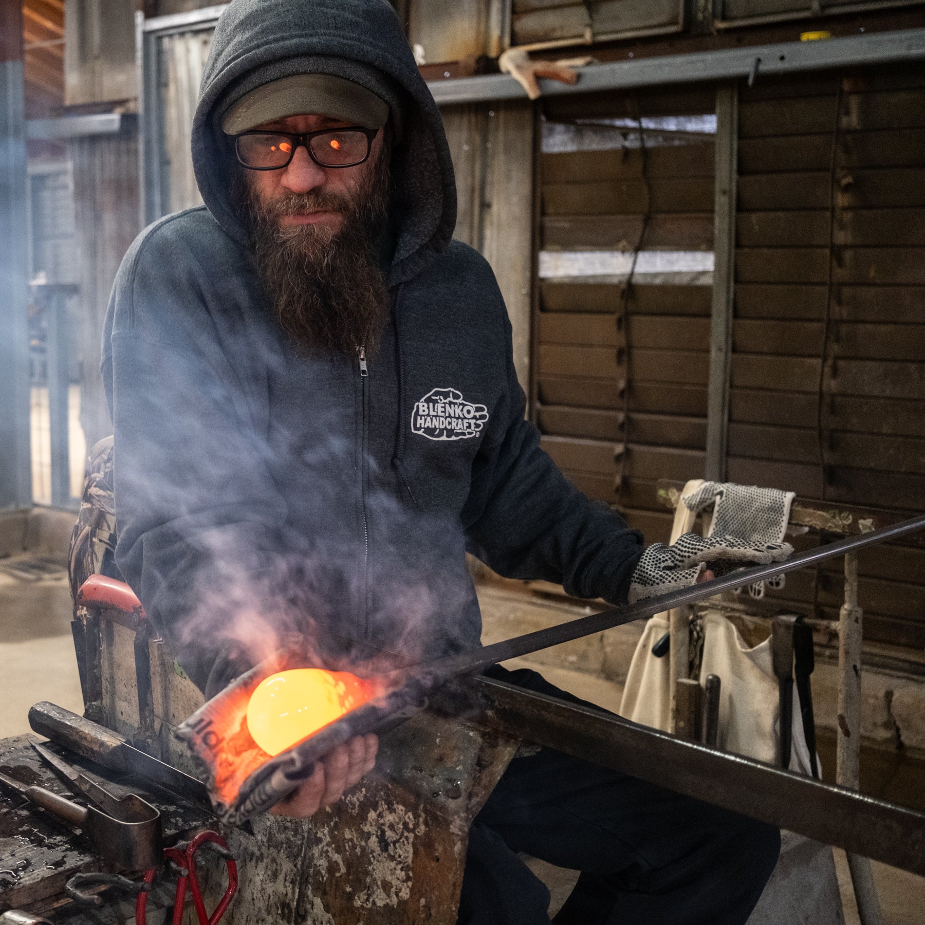 Man in a workshop holding glowing metal in a forge