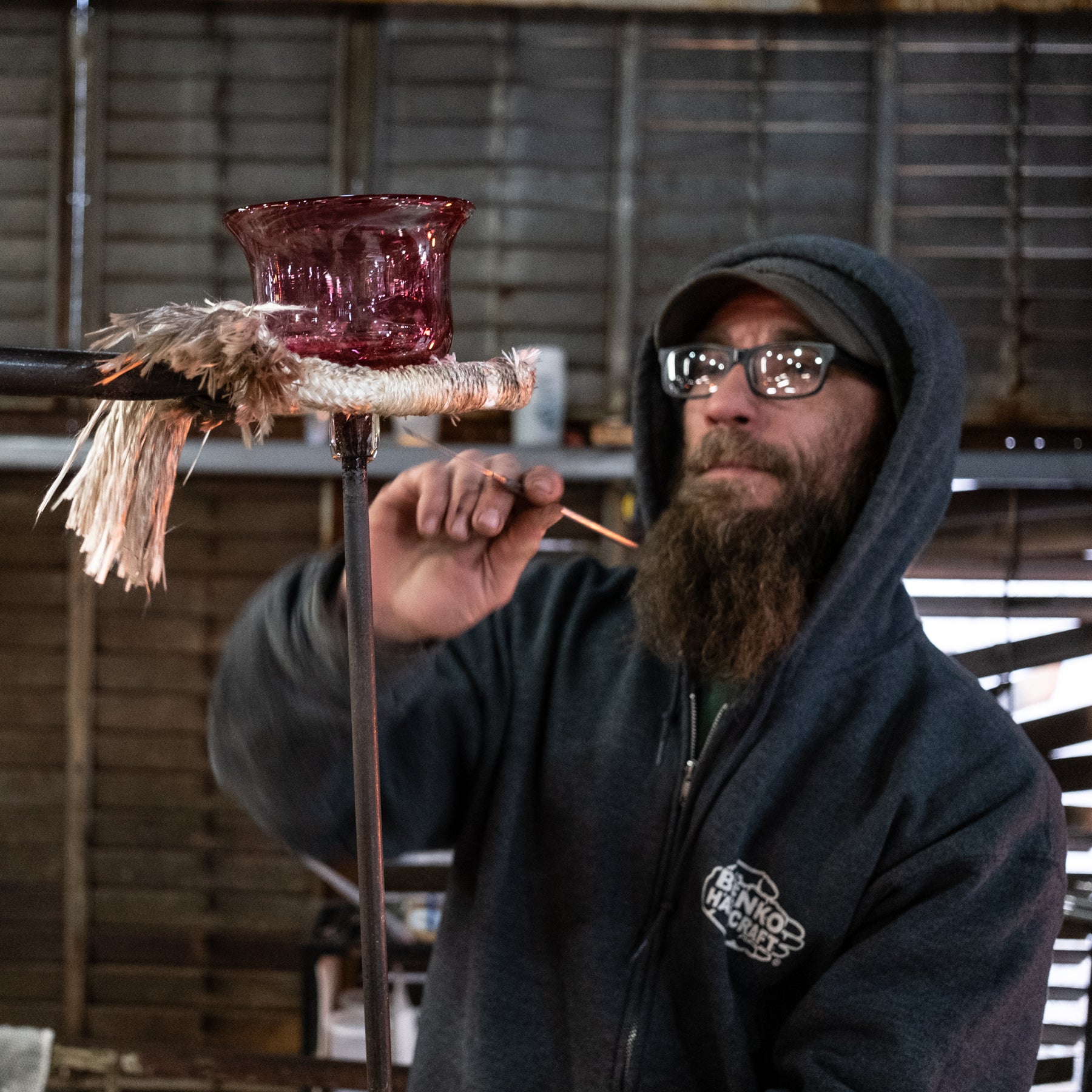 Person working with glass on a hot metal rod in a workshop setting