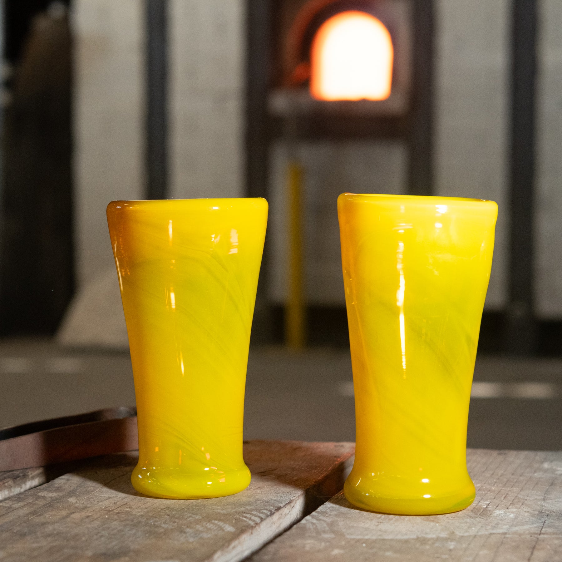 Two yellow glass tumblers on a wooden surface with a blurred background