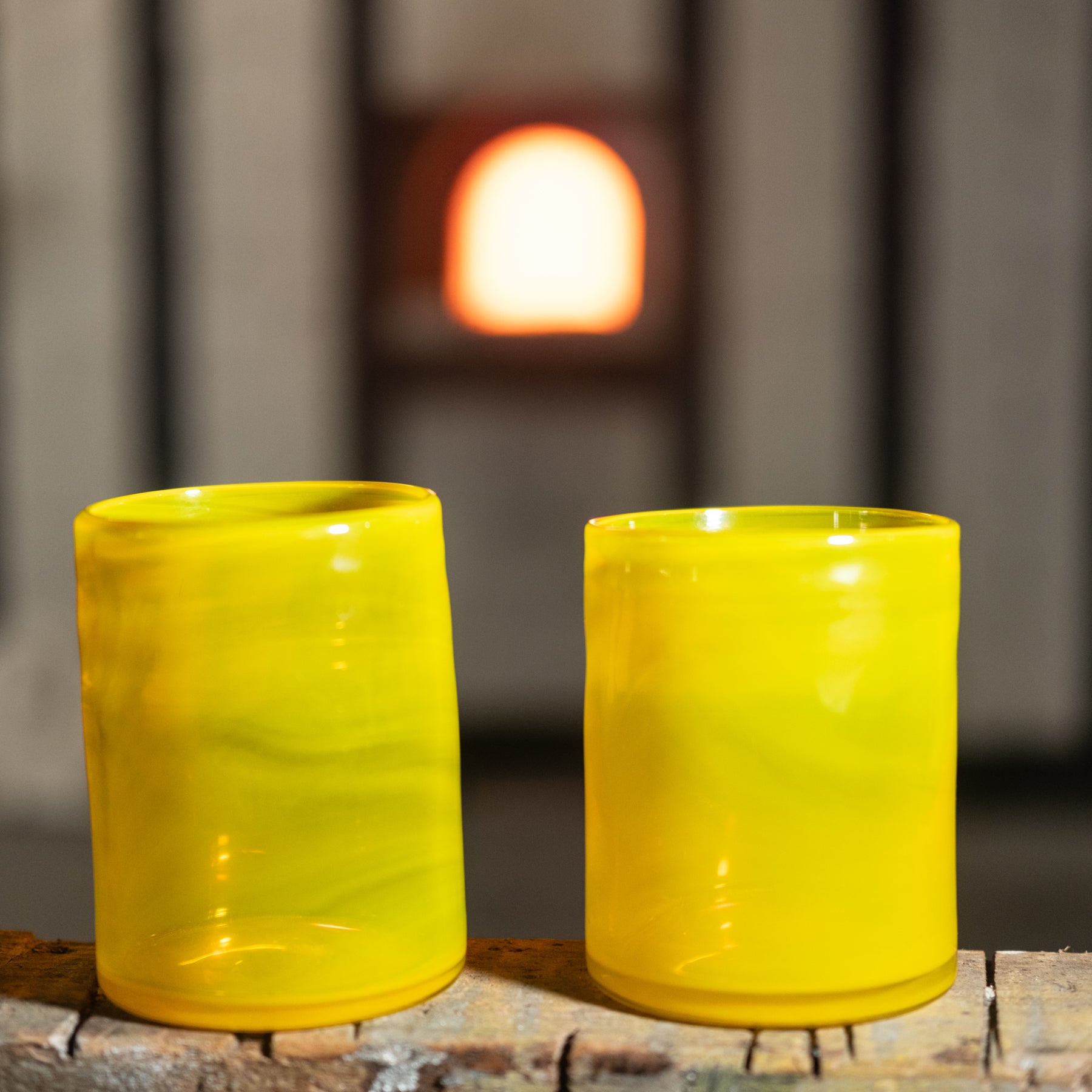 Two yellow glass tumblers on a wooden surface with a blurred background