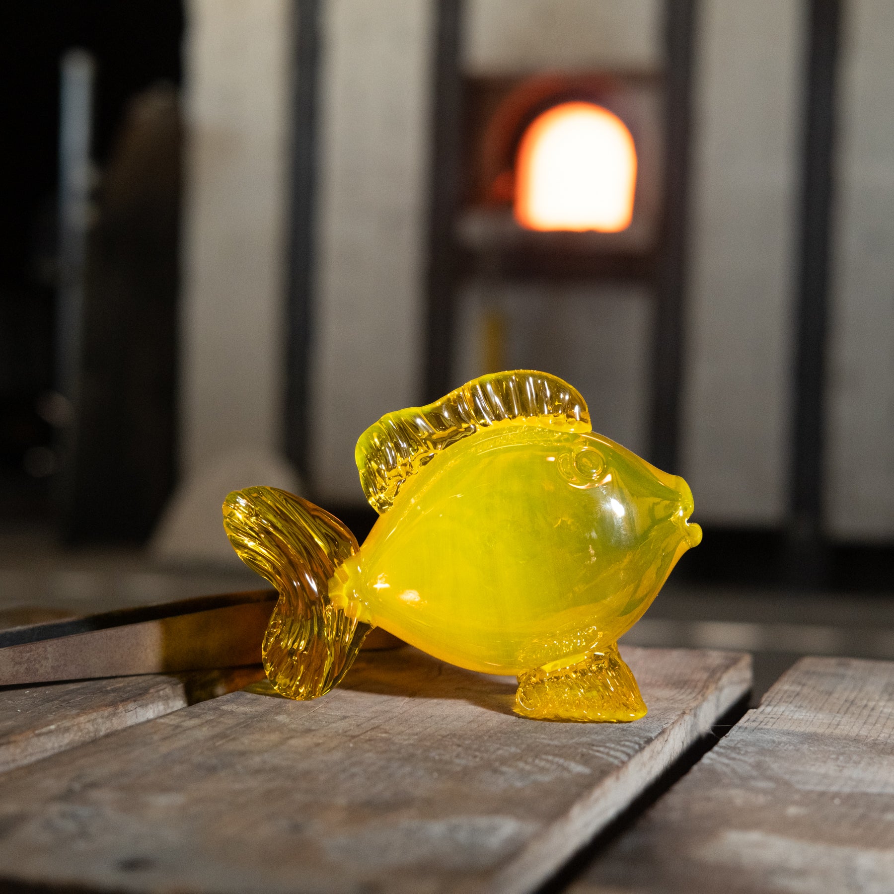 Yellow glass fish figurine on a wooden surface with a blurred background