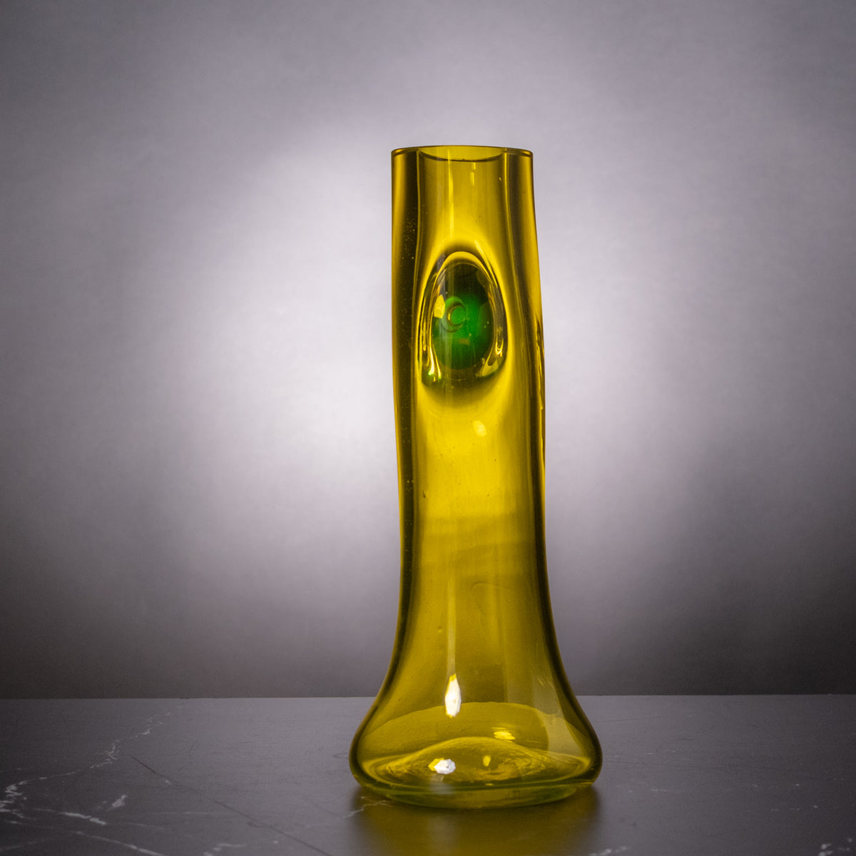 A translucent yellow-green glass vase with a bulbous base and a glossy, wavy vertical texture, standing on a dark surface against a gray gradient background.
