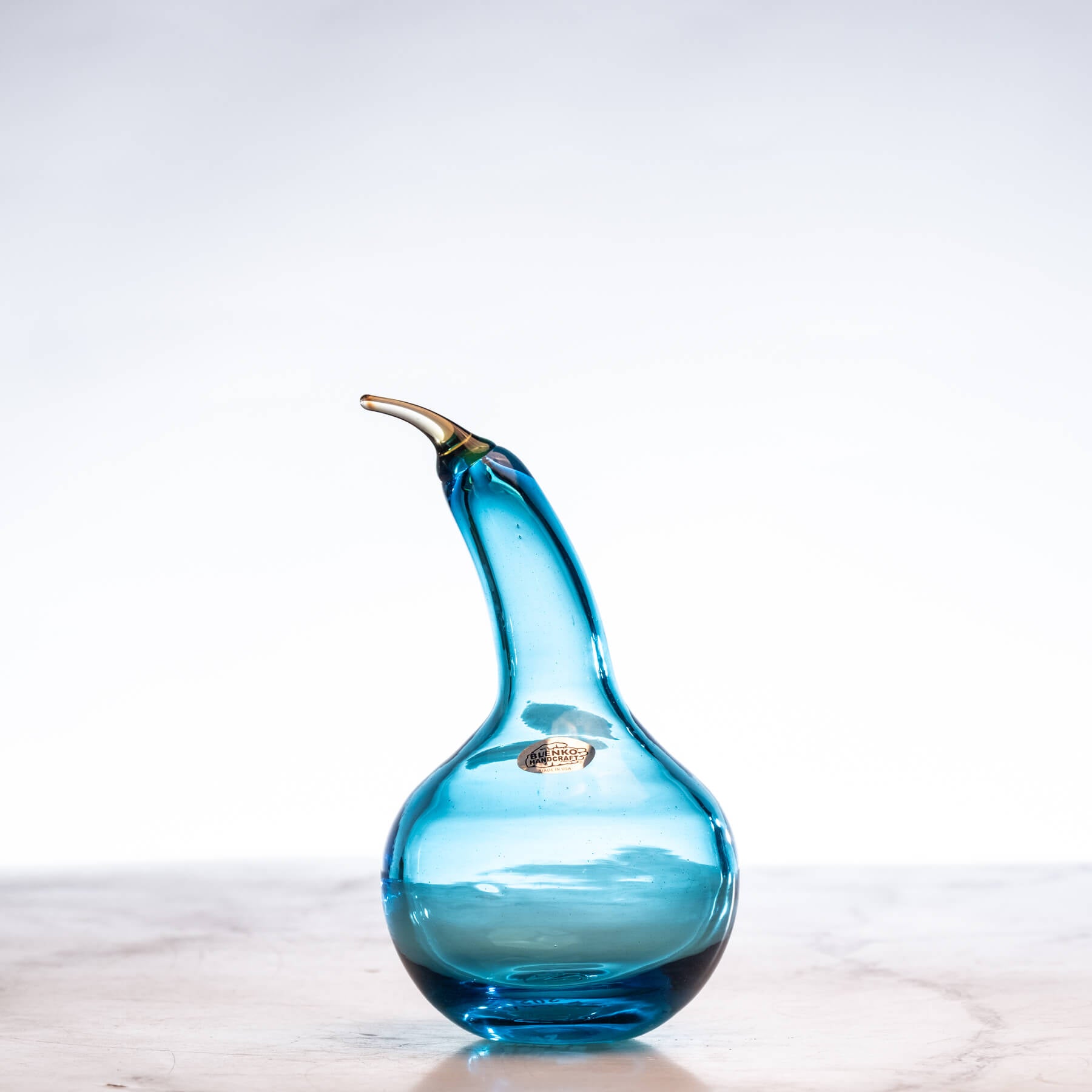 Blue glass pear-shaped vase on a light wooden surface with a white background
