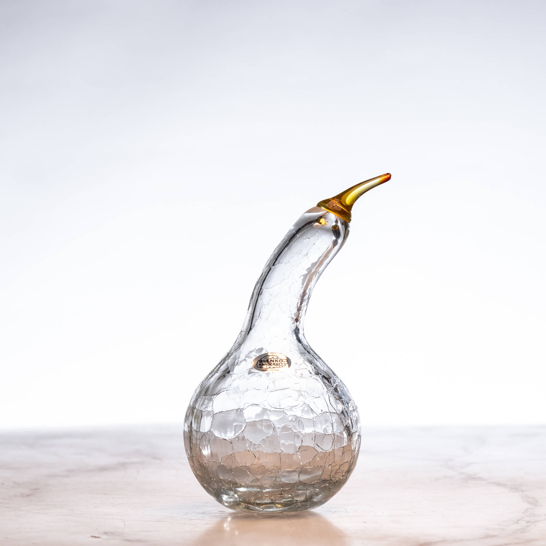Glass duck-shaped object with a gold beak on a light background