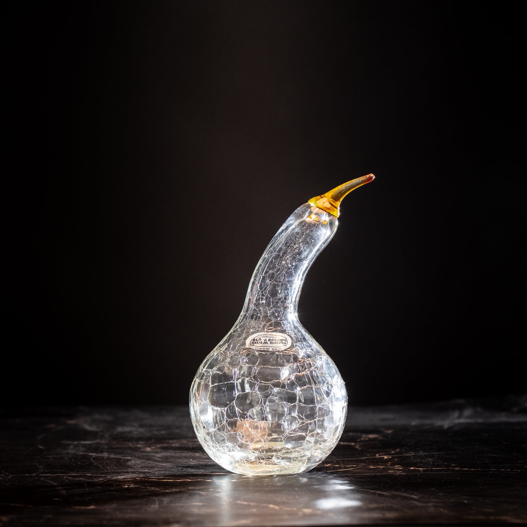 Decorative glass object resembling a gourd with a gold top on a dark background