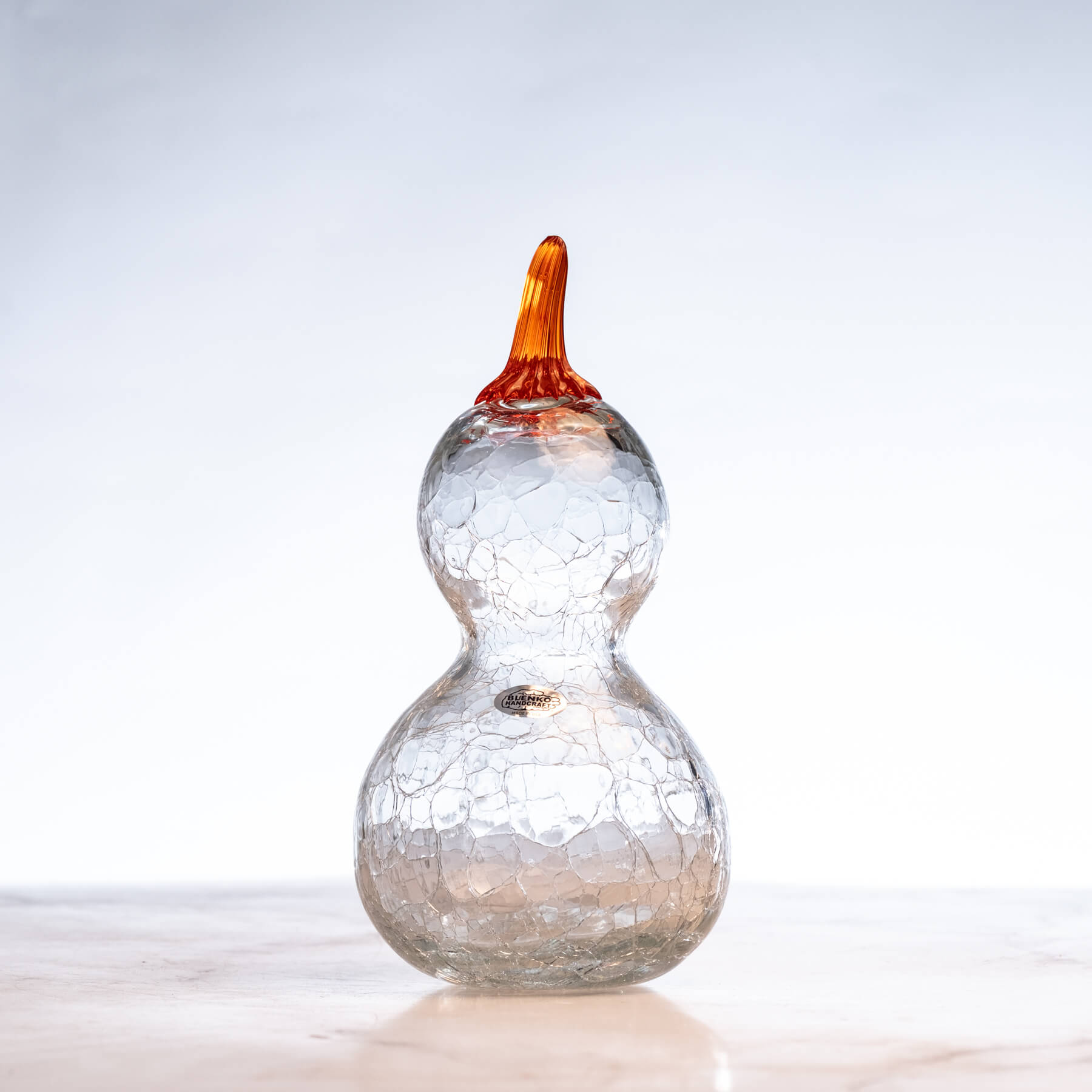 Glass gourd with crackled design and orange stem on a white background