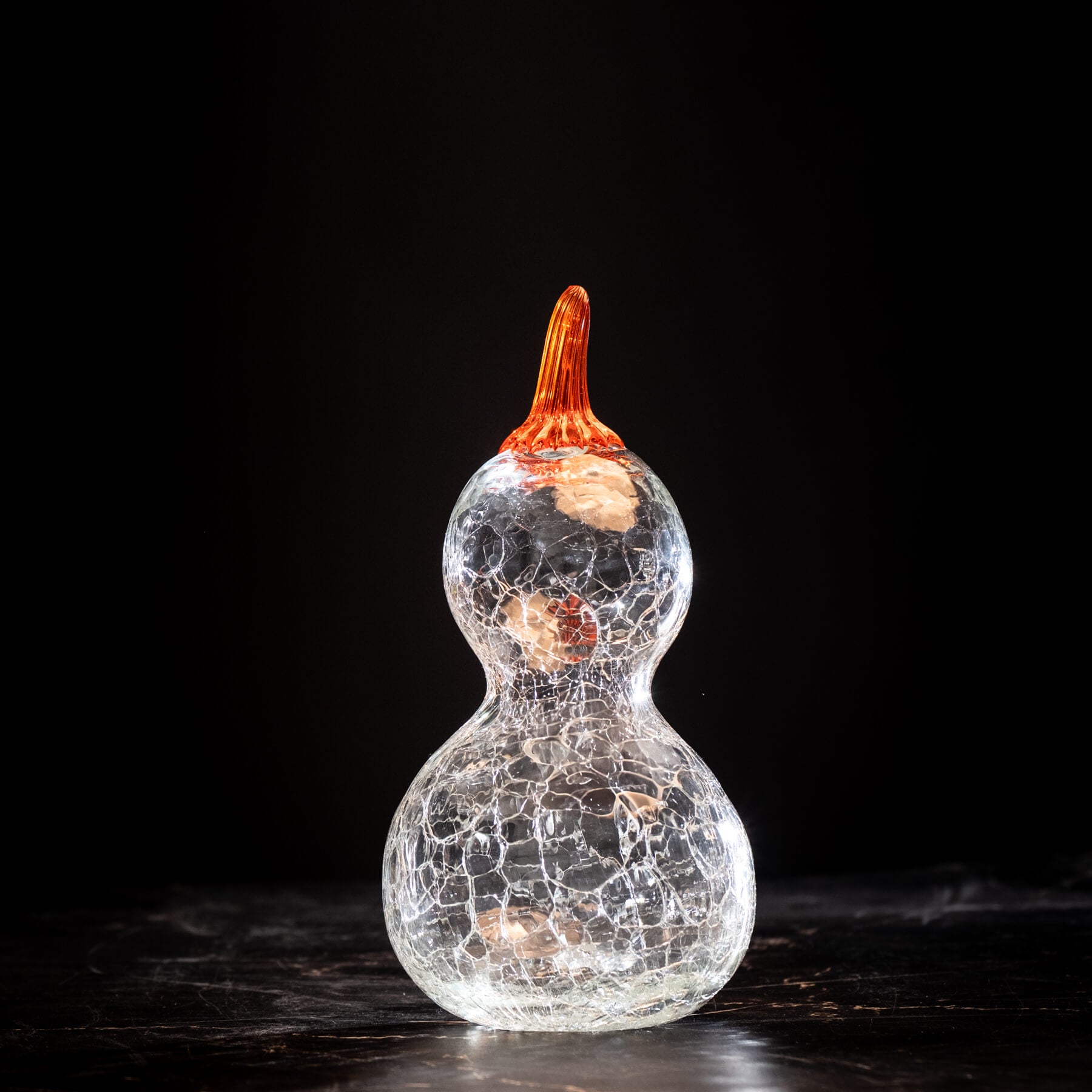 Glass gourd with cracked texture and orange stem on a dark background