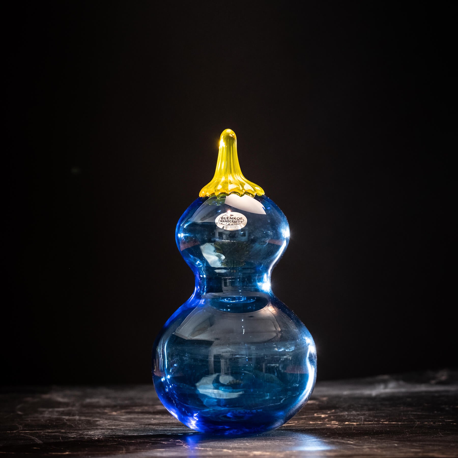 Blue glass calabash gourd a yellow stem on a dark background