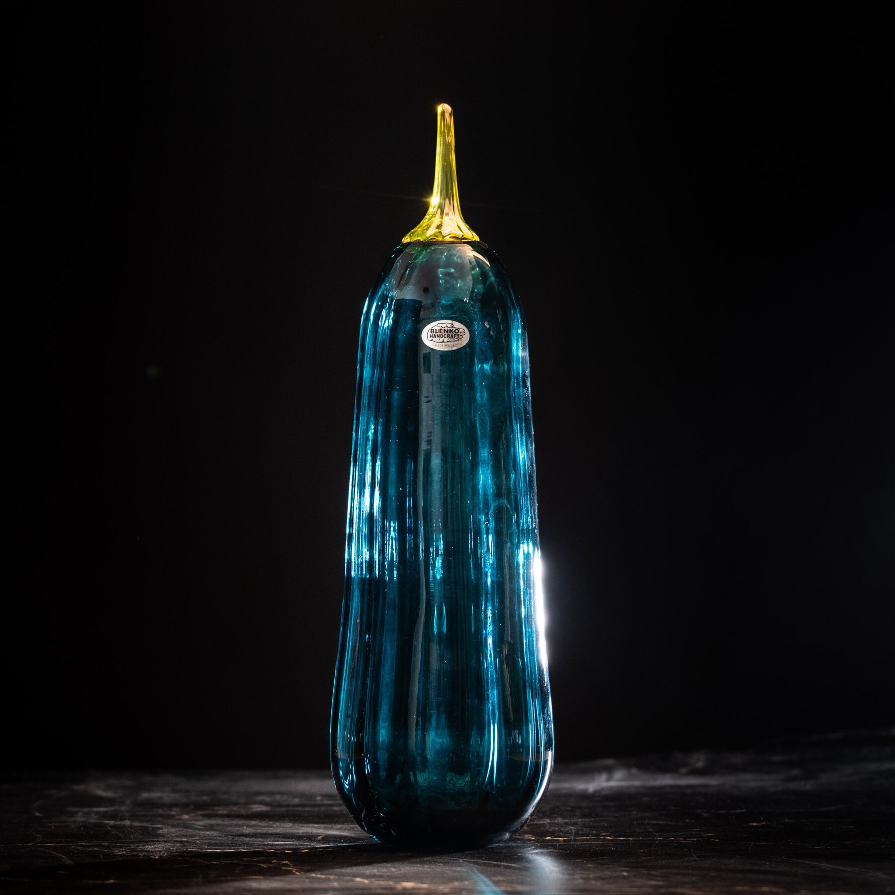 Blue glass tall pumpkin with a yellow stem on a dark background