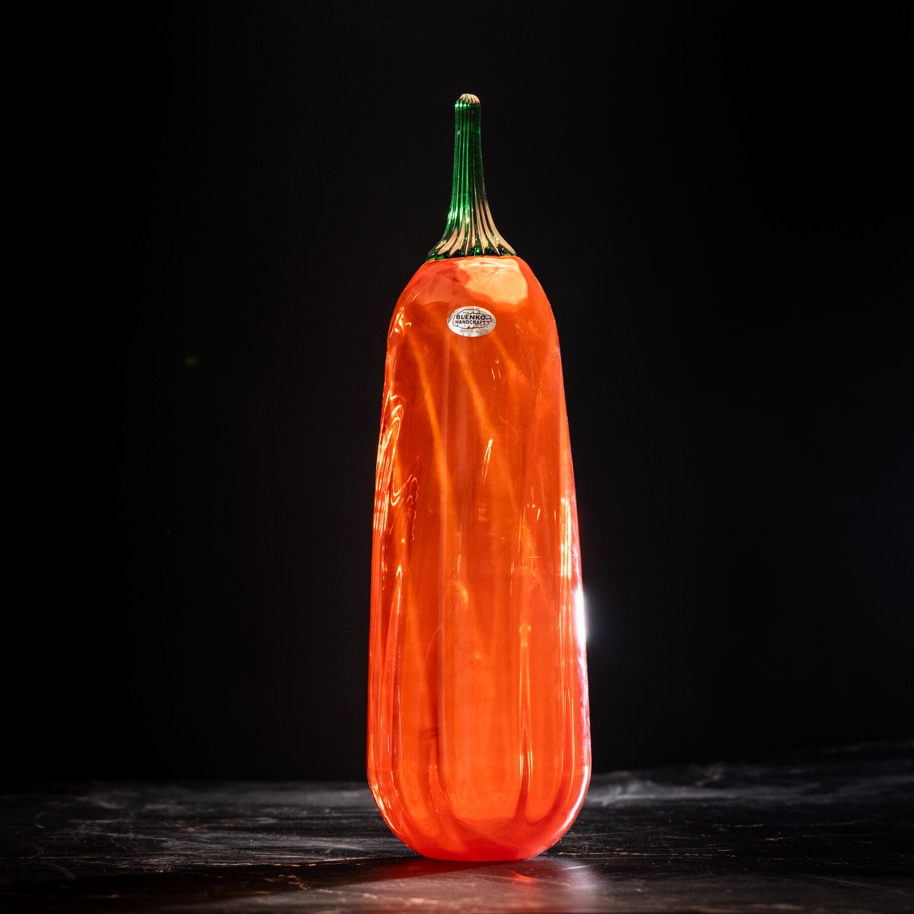 Orange glass gourd with green stem on a dark background