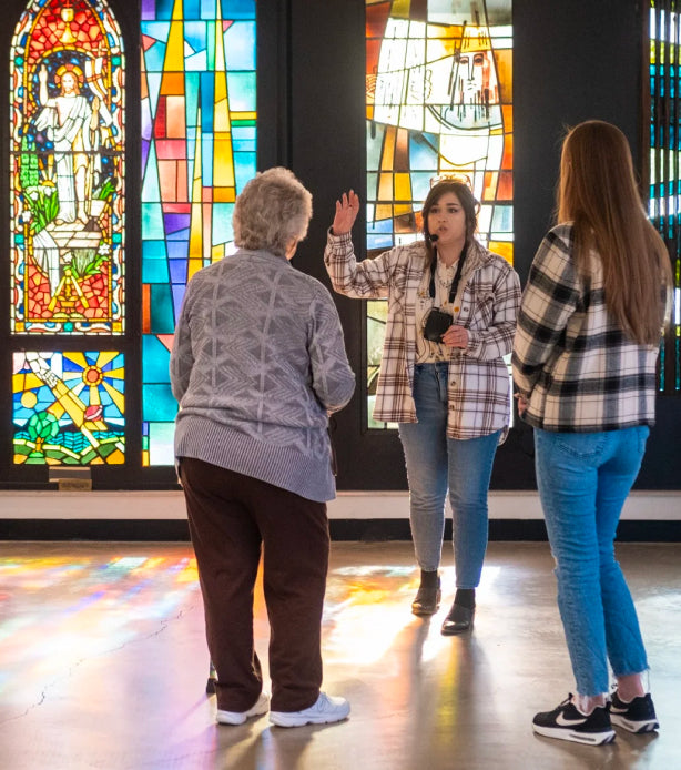 Tour guide and two guests in front of a colorful stained glass window