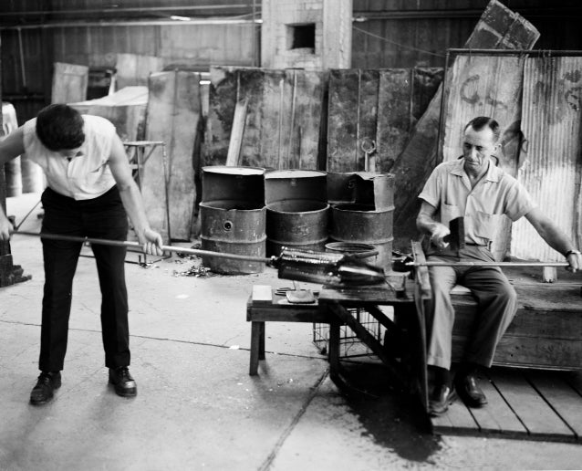 A historical photos of two men making a large glass vessel at Blenko Glass Factory.
