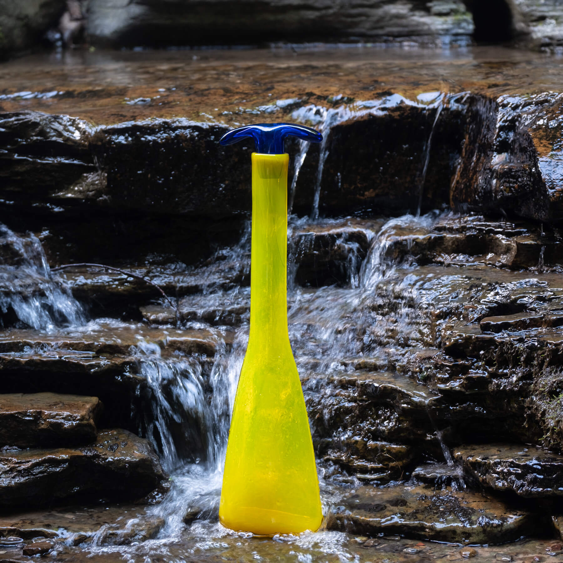 Yellow bottle with blue cap on a rocky stream background