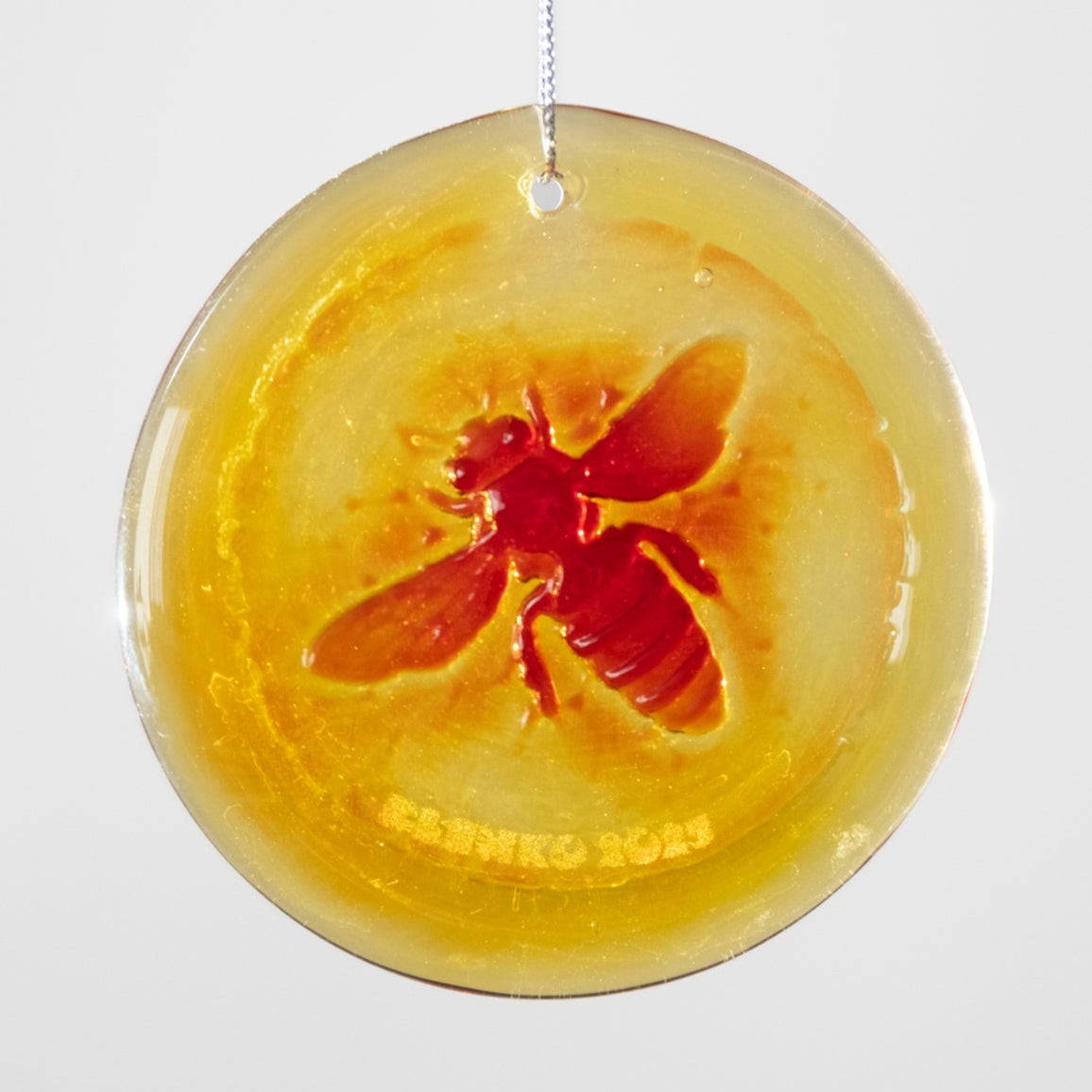 Round amber-colored object with a red bee design on a white background
