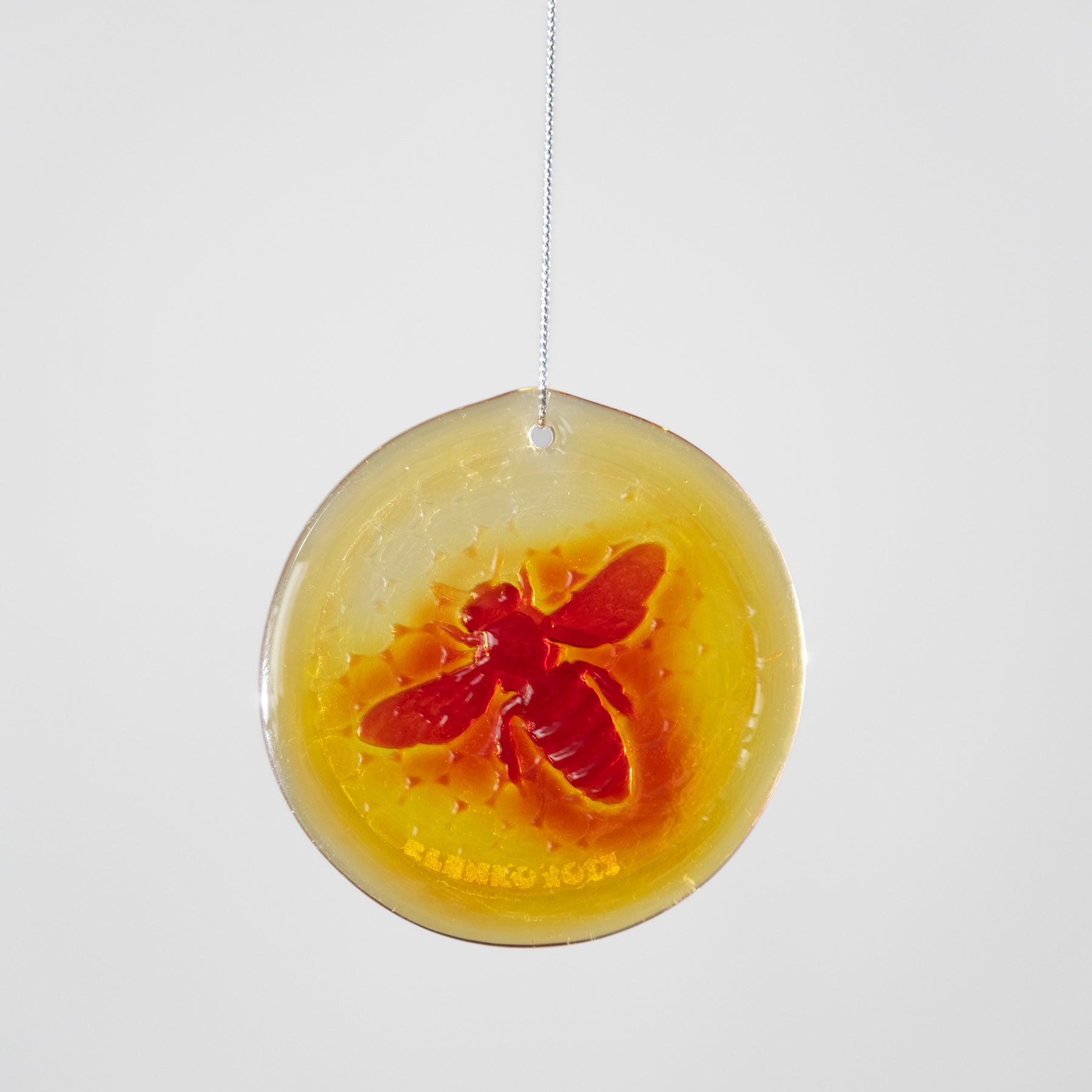 Round yellow and orange hanging ornament with a red bee design on a white background