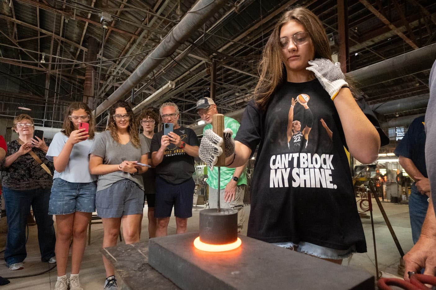 Person working with a hot object in a workshop setting, surrounded by onlookers.