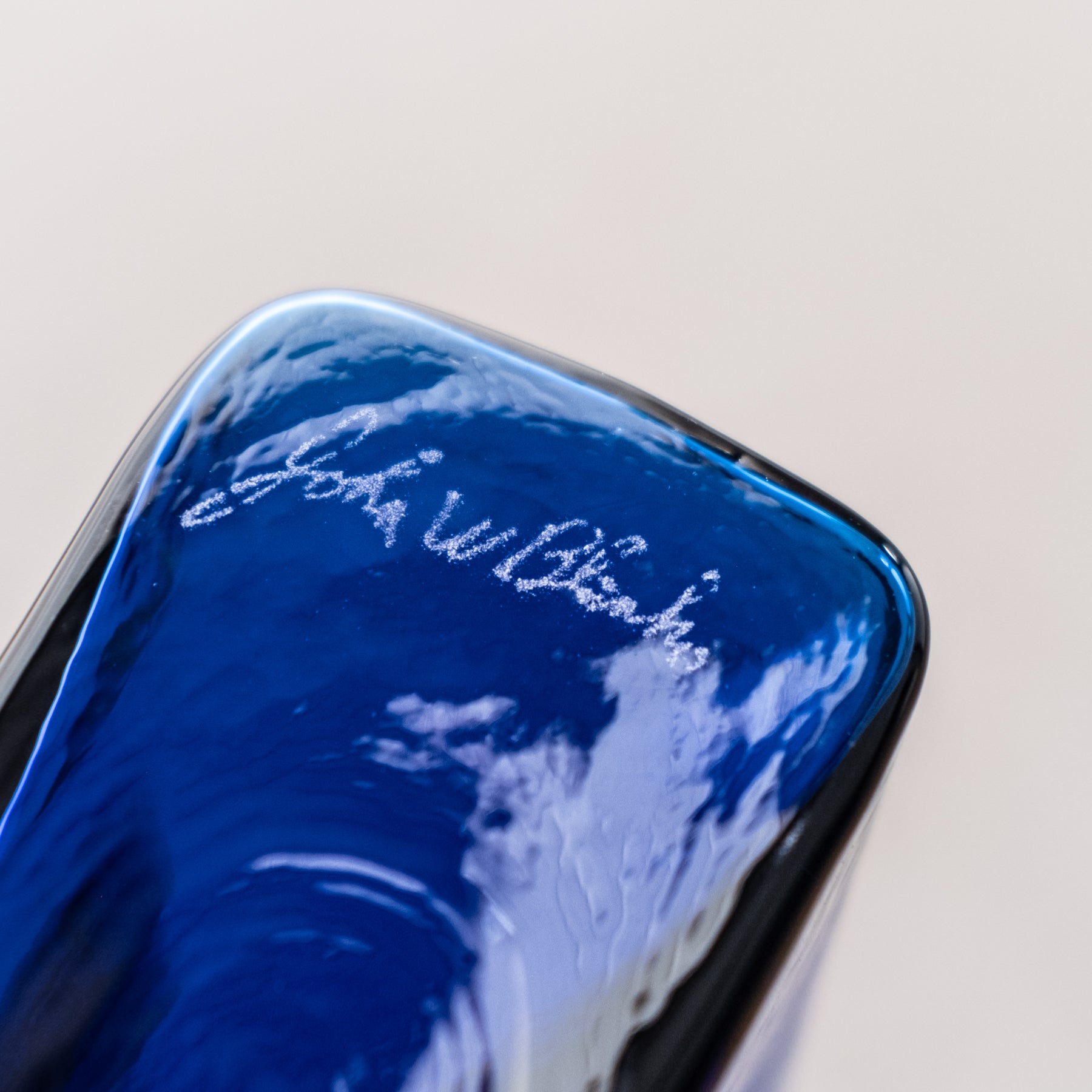 A close-up of a blue glass item with a sandblasted signature in white text.