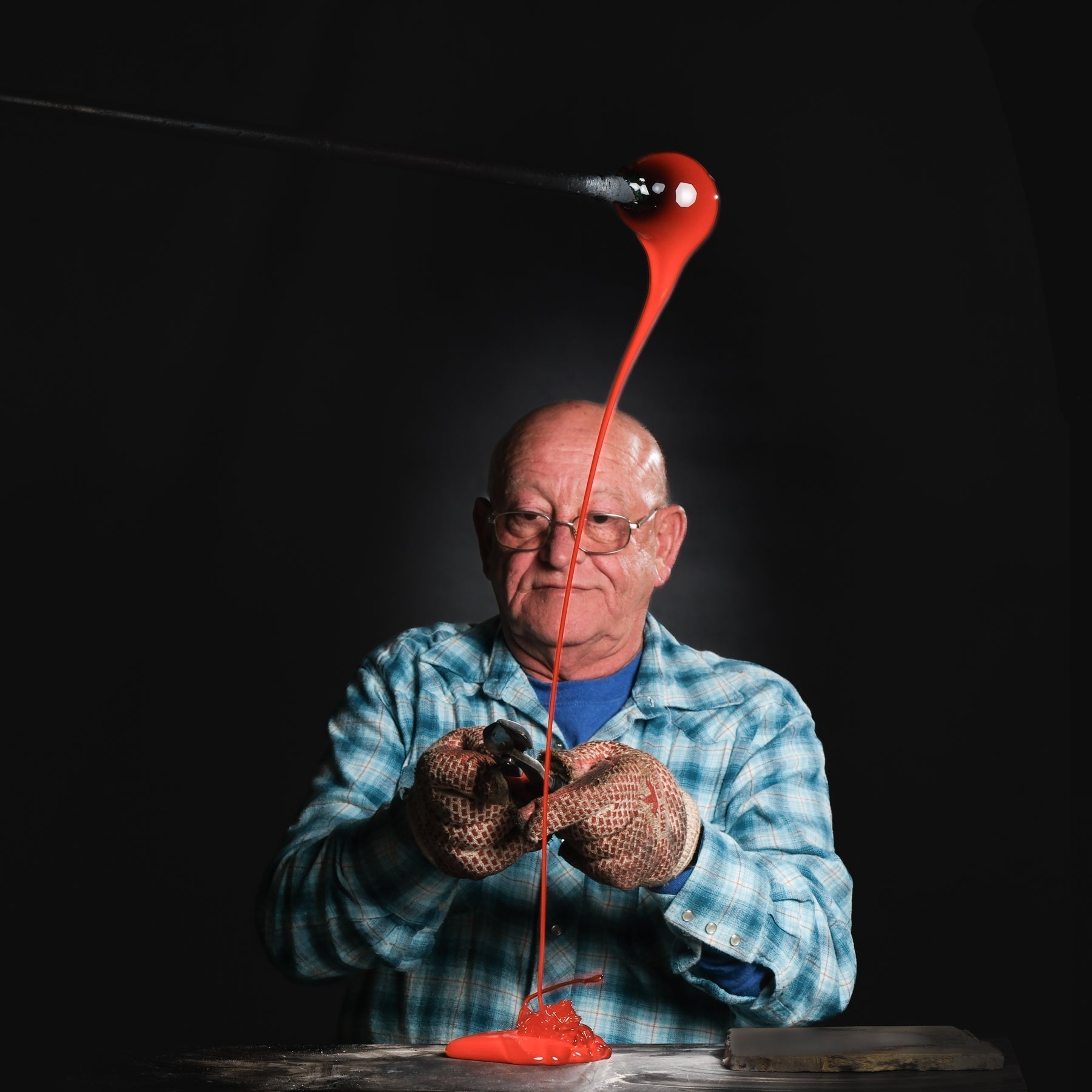 Person holding molten red glass against a dark background
