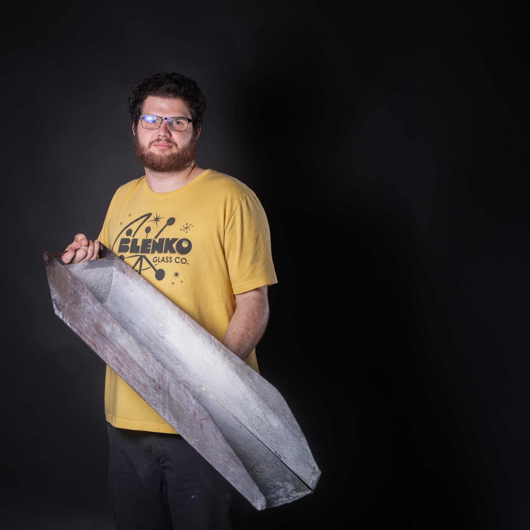 Worker in yellow shirt holding a piece of metal on black background