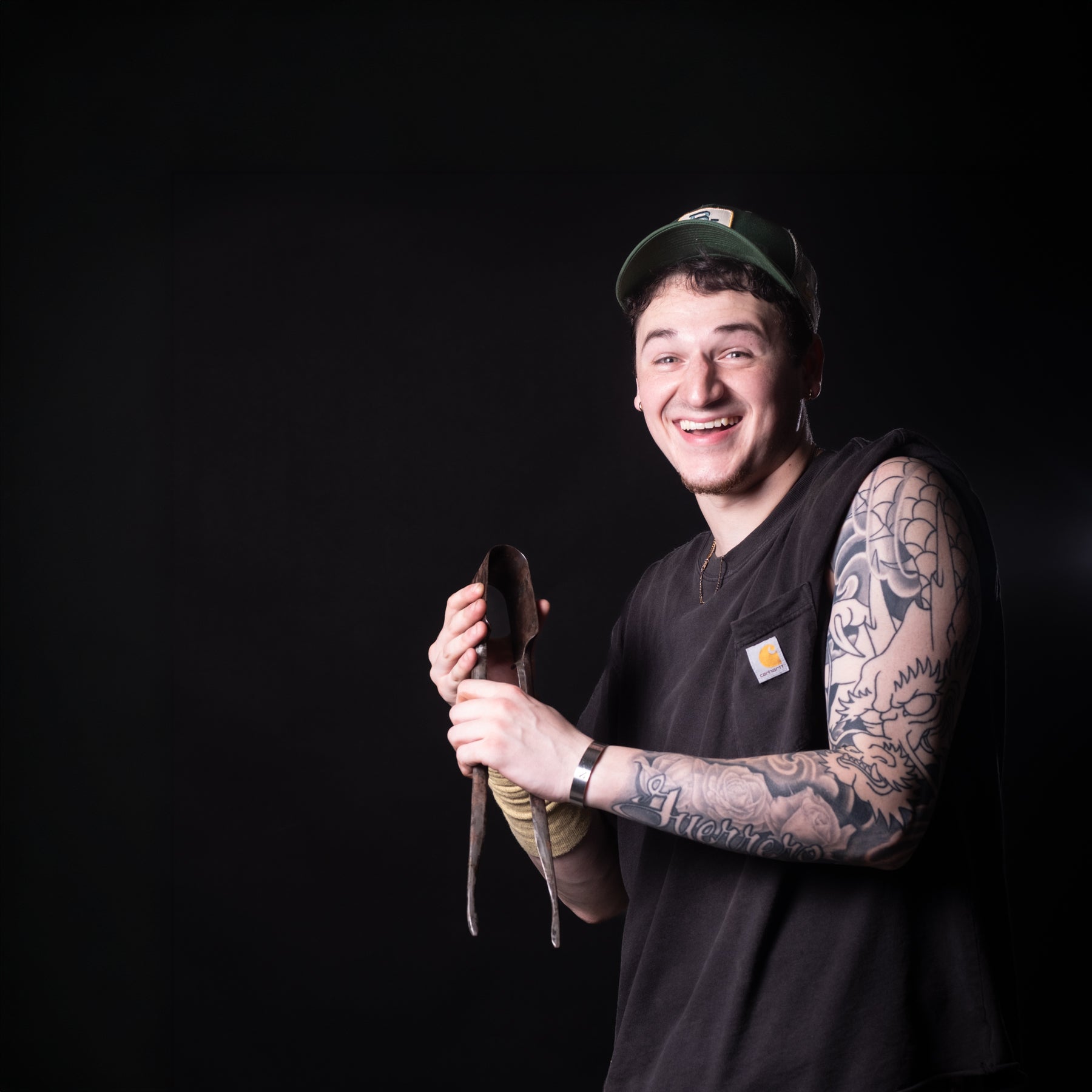Man with tattoos holding a tool against a black background