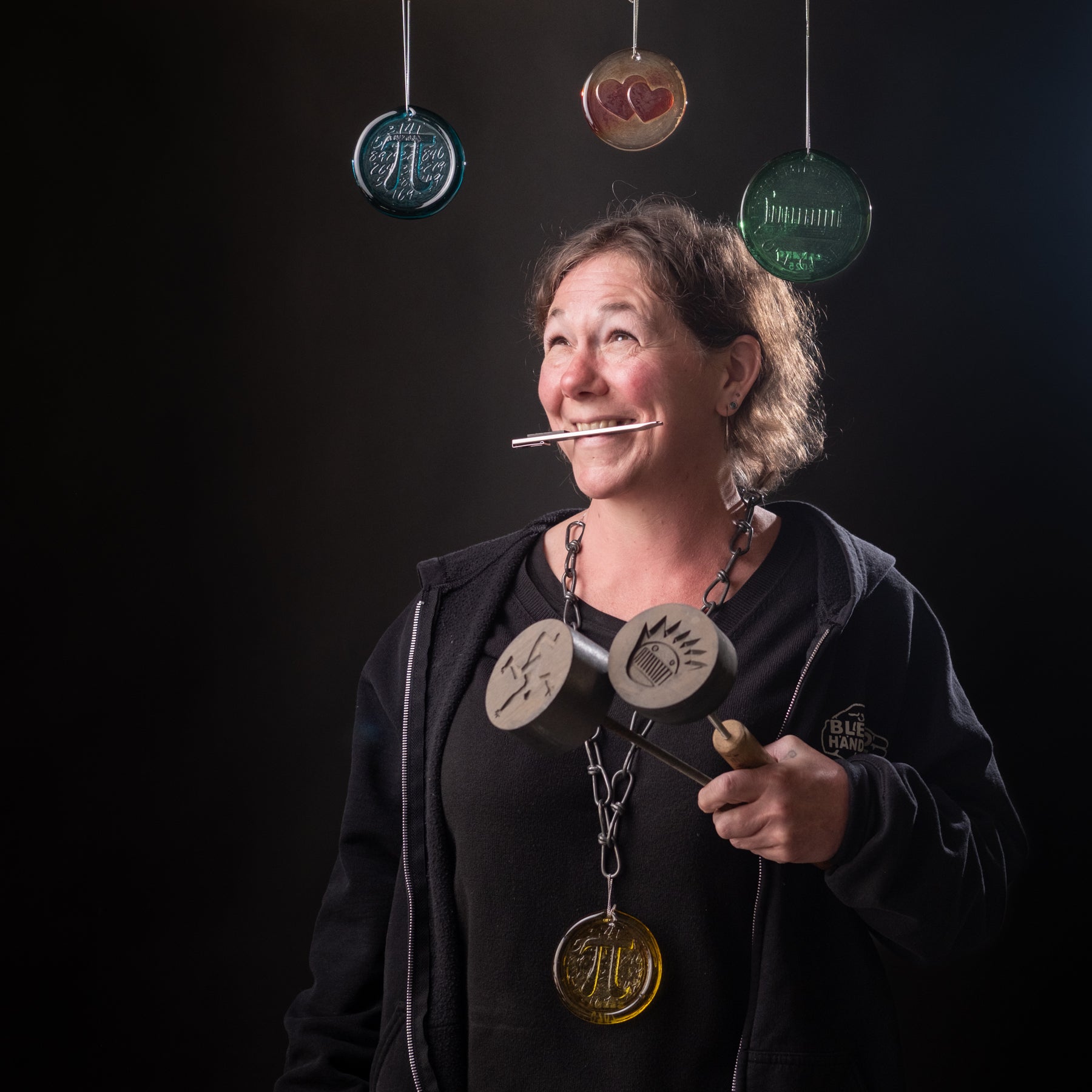 Person holding a tool with hanging metal objects against a dark background
