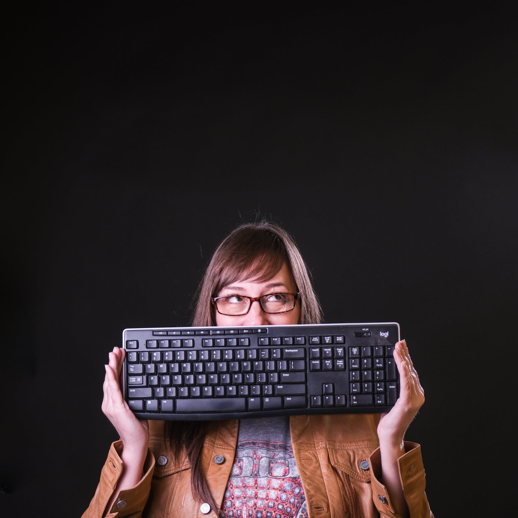 Person holding a keyboard in front of their face on a black background