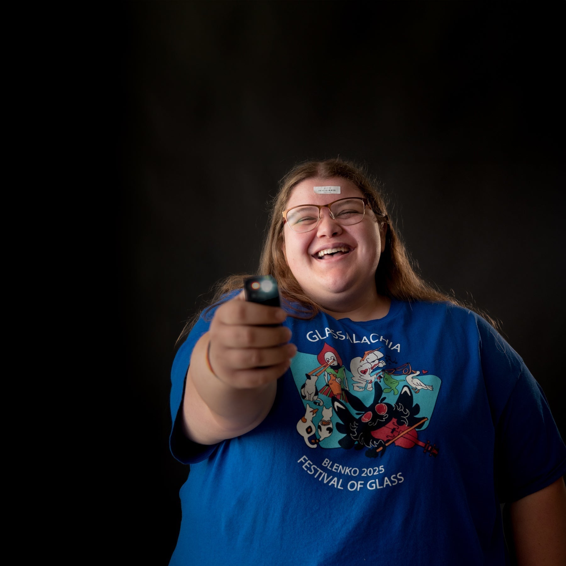 Person wearing a blue t-shirt with a graphic design, holding a small object against a black background